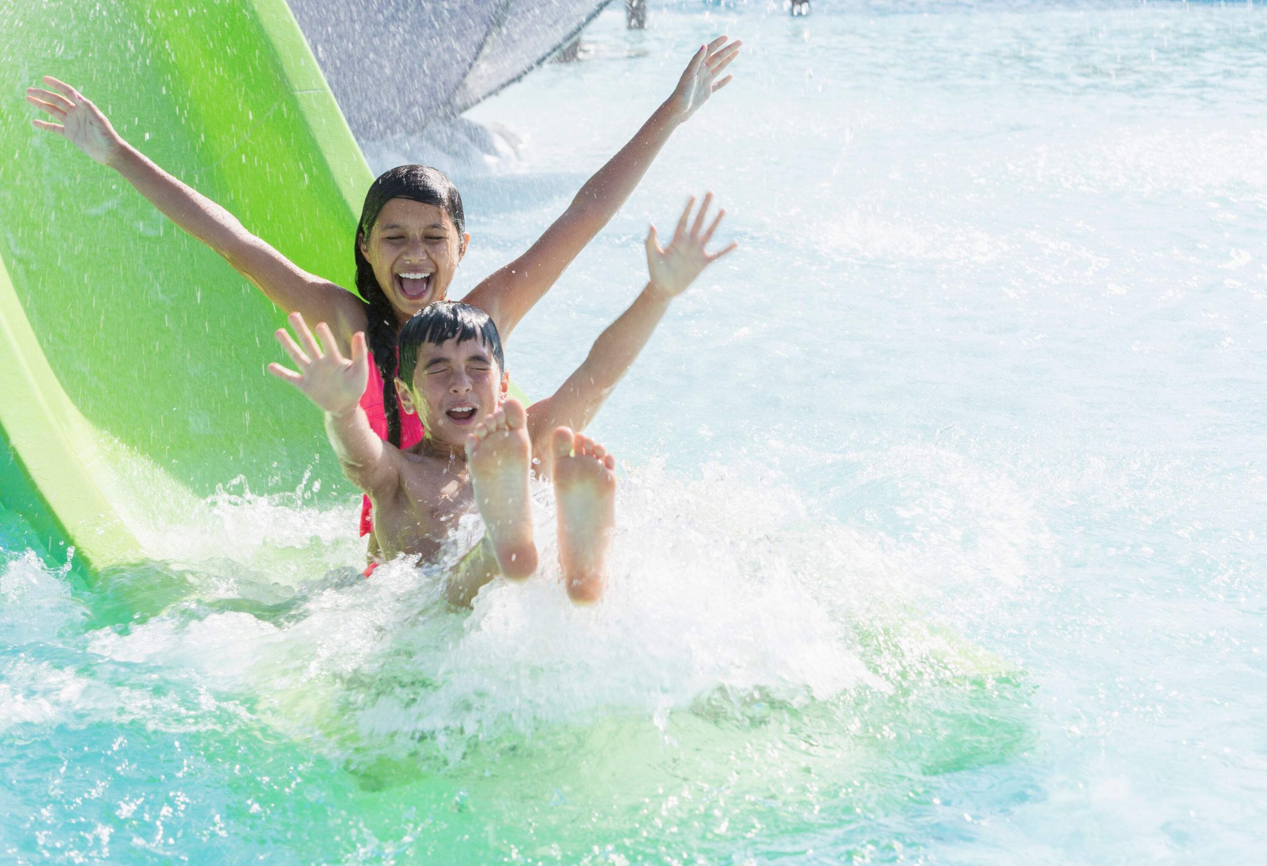 A little boy and girl slide down a slide into a pool.