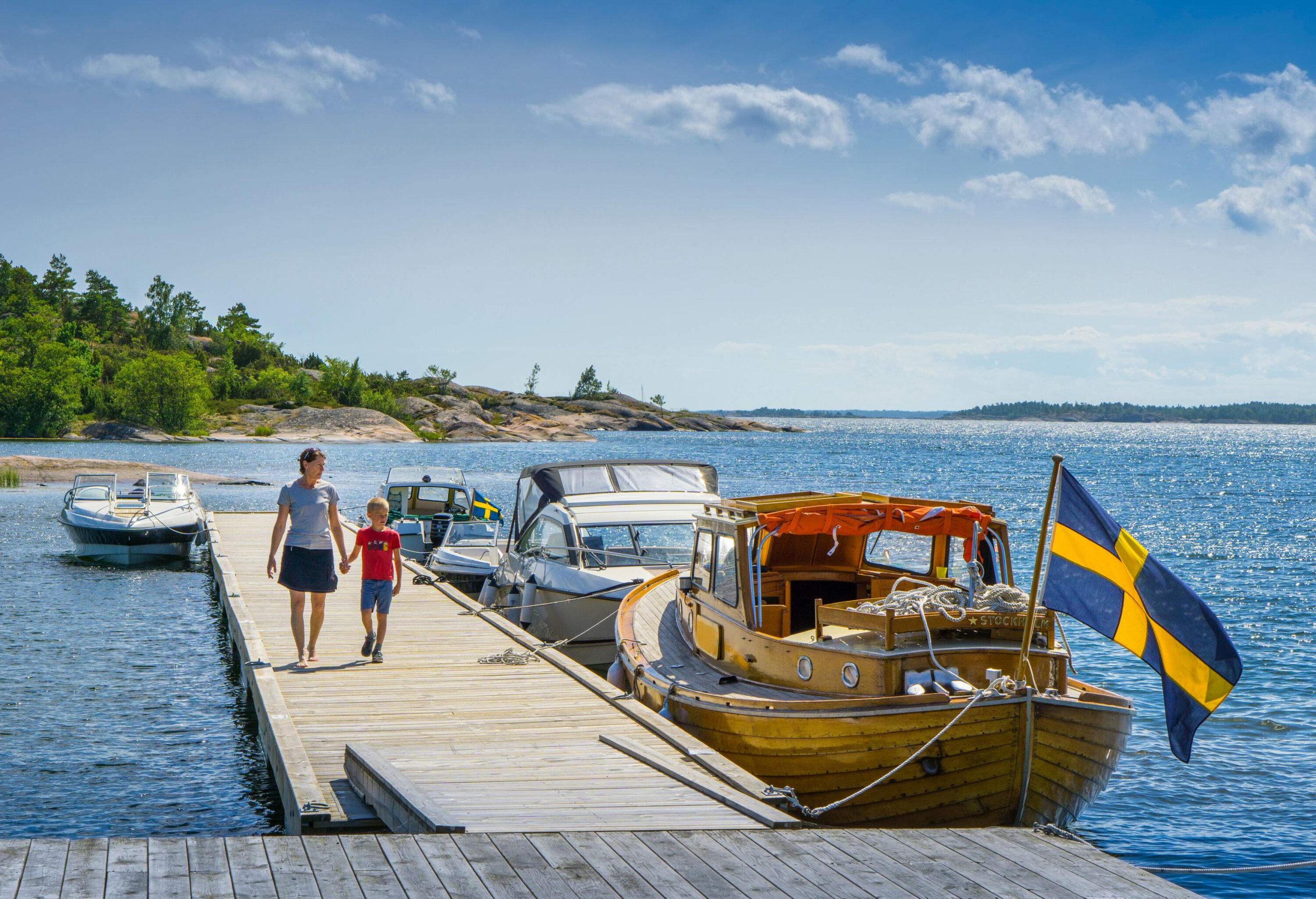 A mother and son strolling down a pier with docked boats on the side.