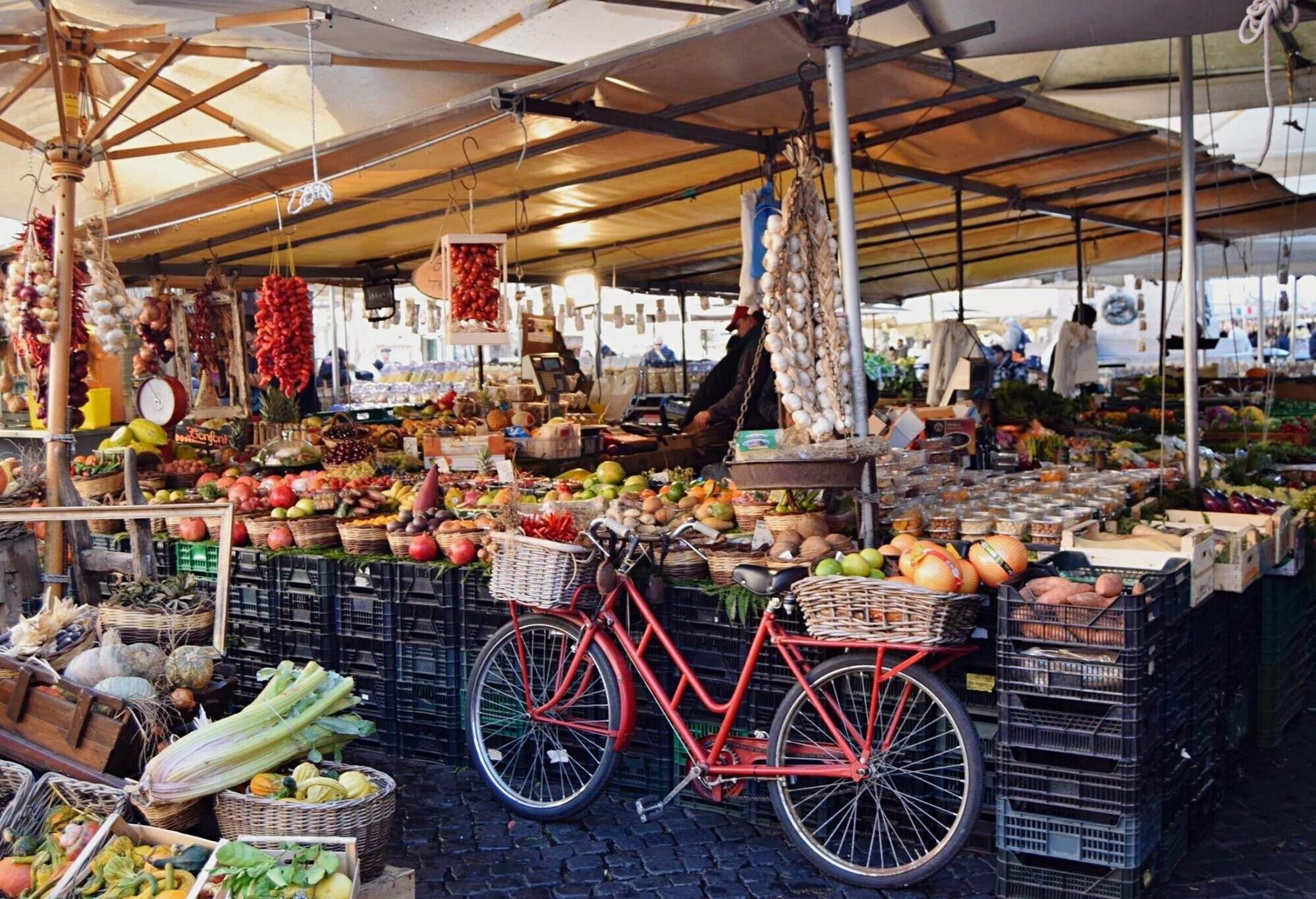 A tent with a display of assorted fruits for sale beside a bicycle with baskets full of products.