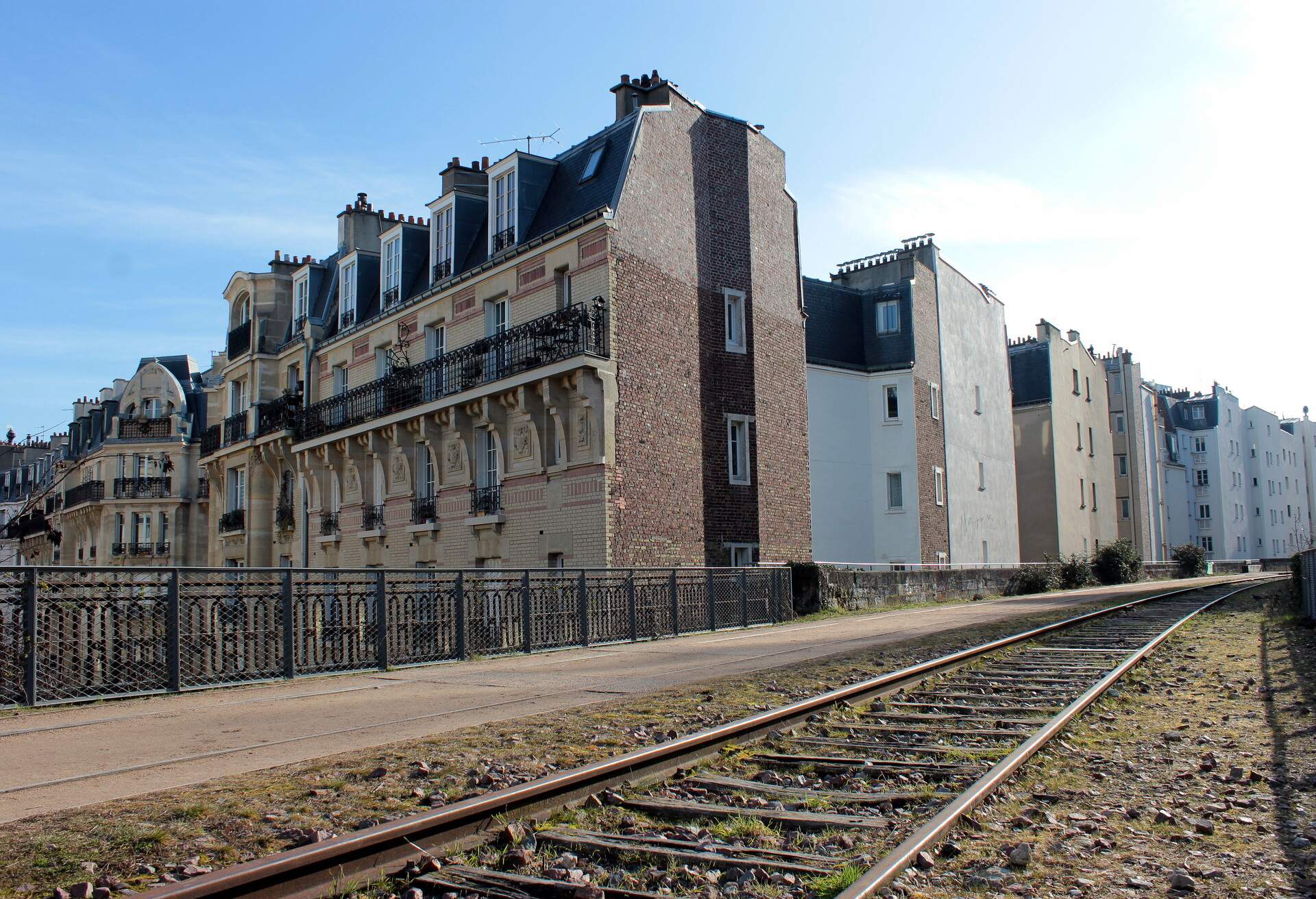 Fence-enclosed residential buildings next to the train tracks.