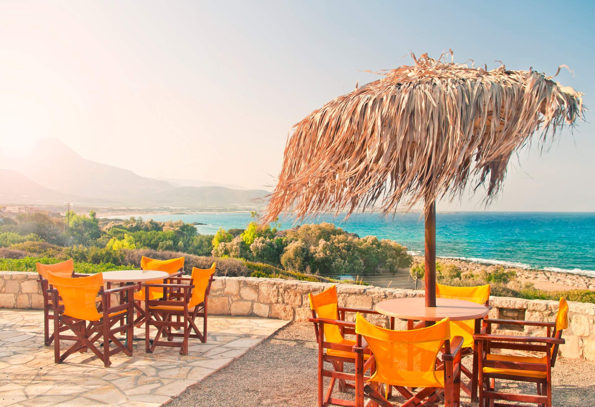 two tables with a palm leave parasol on restaurant balcony with sea and mountain view in early morning, Falasarna beach, Crete, Greece