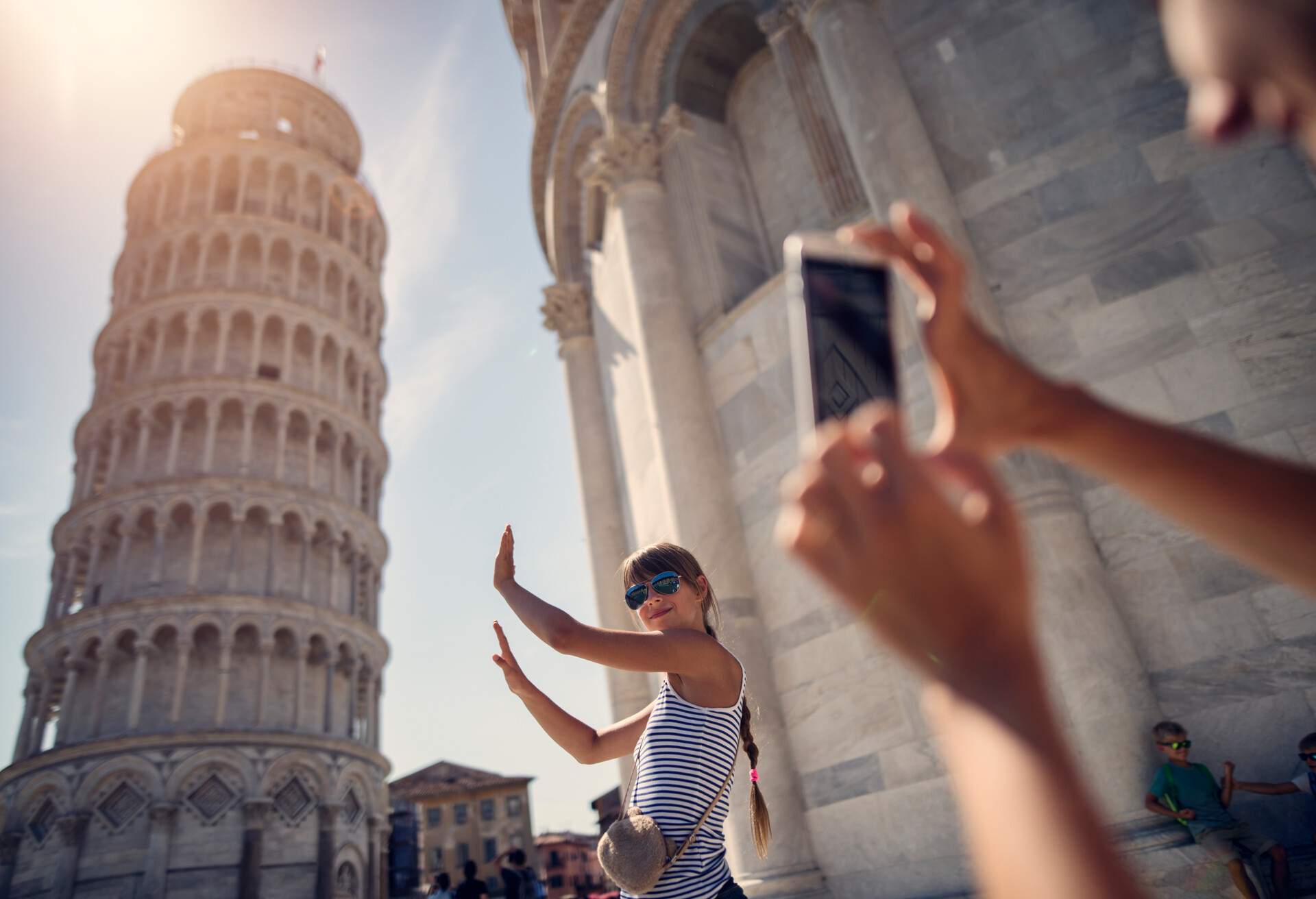 Family sightseeing Pisa, Italy. Teenage girl is posing by the leaning tower of Pisa.  Mother is taking photos and the bored boys are fighting in the background..Kids are aged 8 and 11..Nikon D810