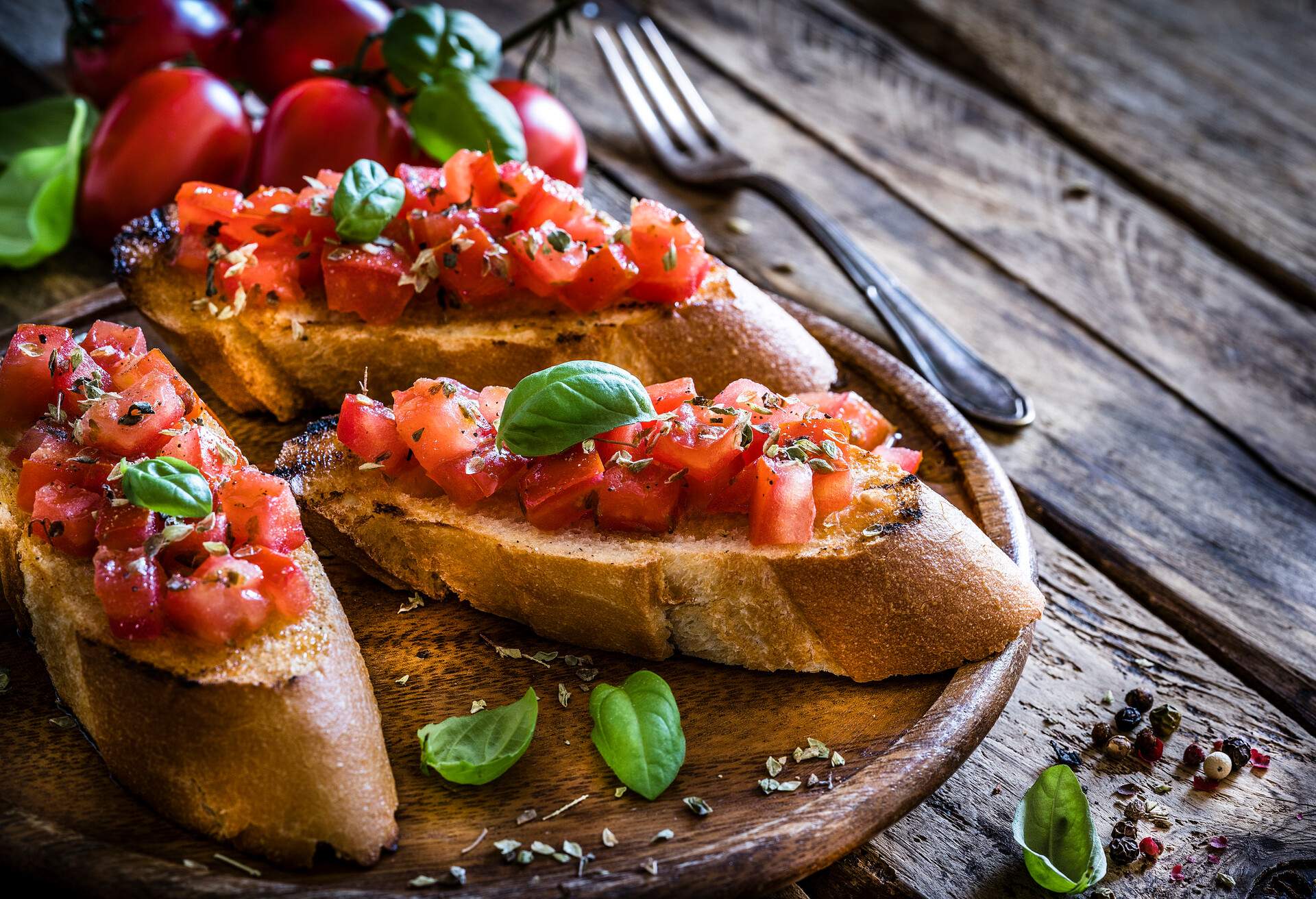 Italian food: homemade bruschetta ready to eat shot on rustic wooden table. Olive oil, tomatoes and peppercorns complete the composition. Predominant colors are red and brown. XXXL 42Mp studio photo taken with Sony A7rii and Sony FE 90mm f2.8 macro G OSS lens