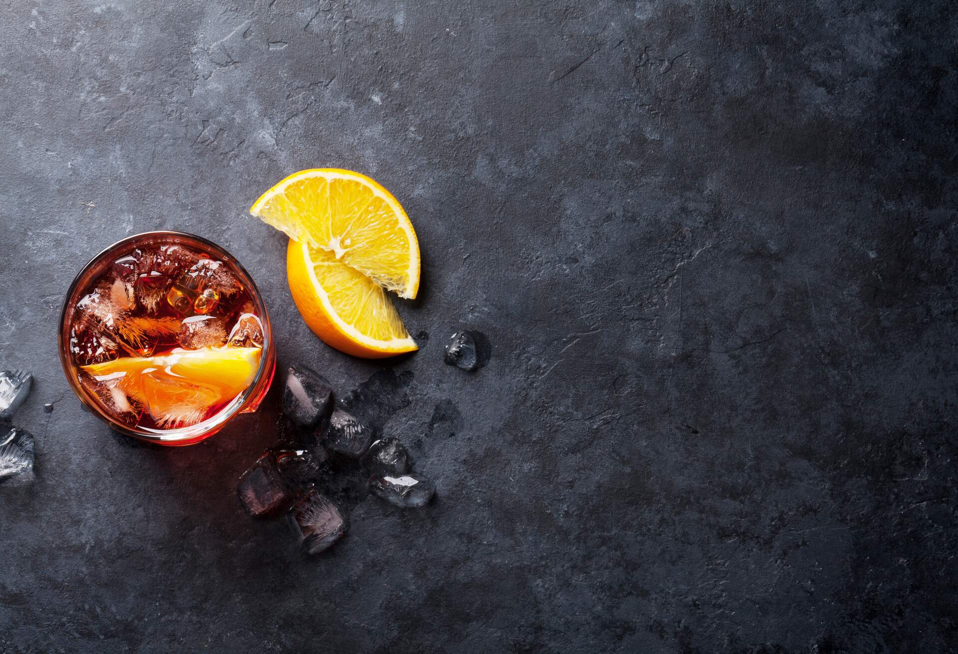 A glass of ice-cold negroni with orange wedges on a black table.