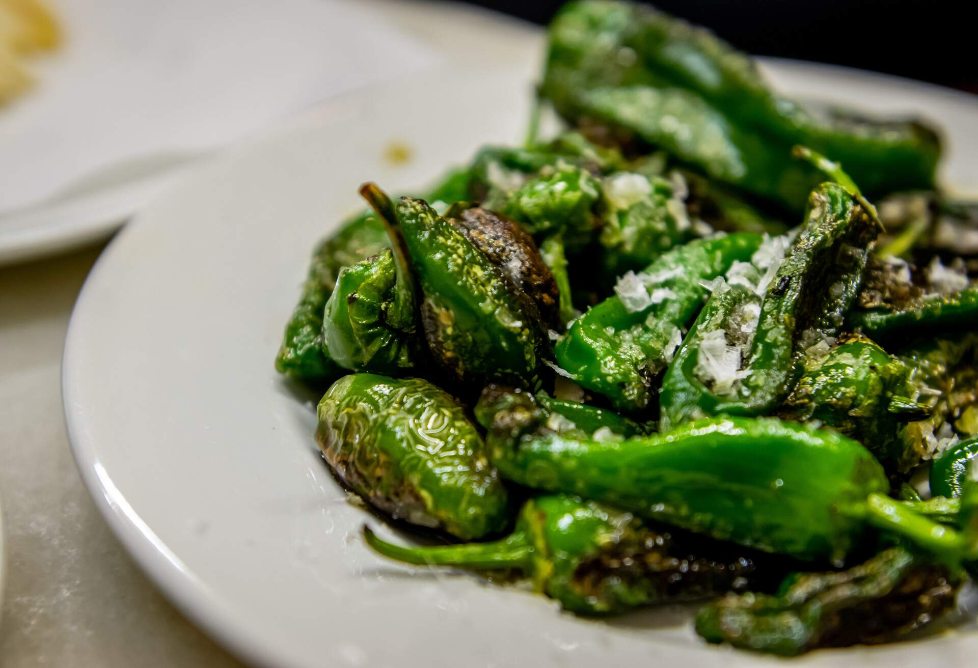 Delicious Padrón peppers, glistening with olive oil and sprinkled with coarse sea salt, are enticingly arranged on a plate.