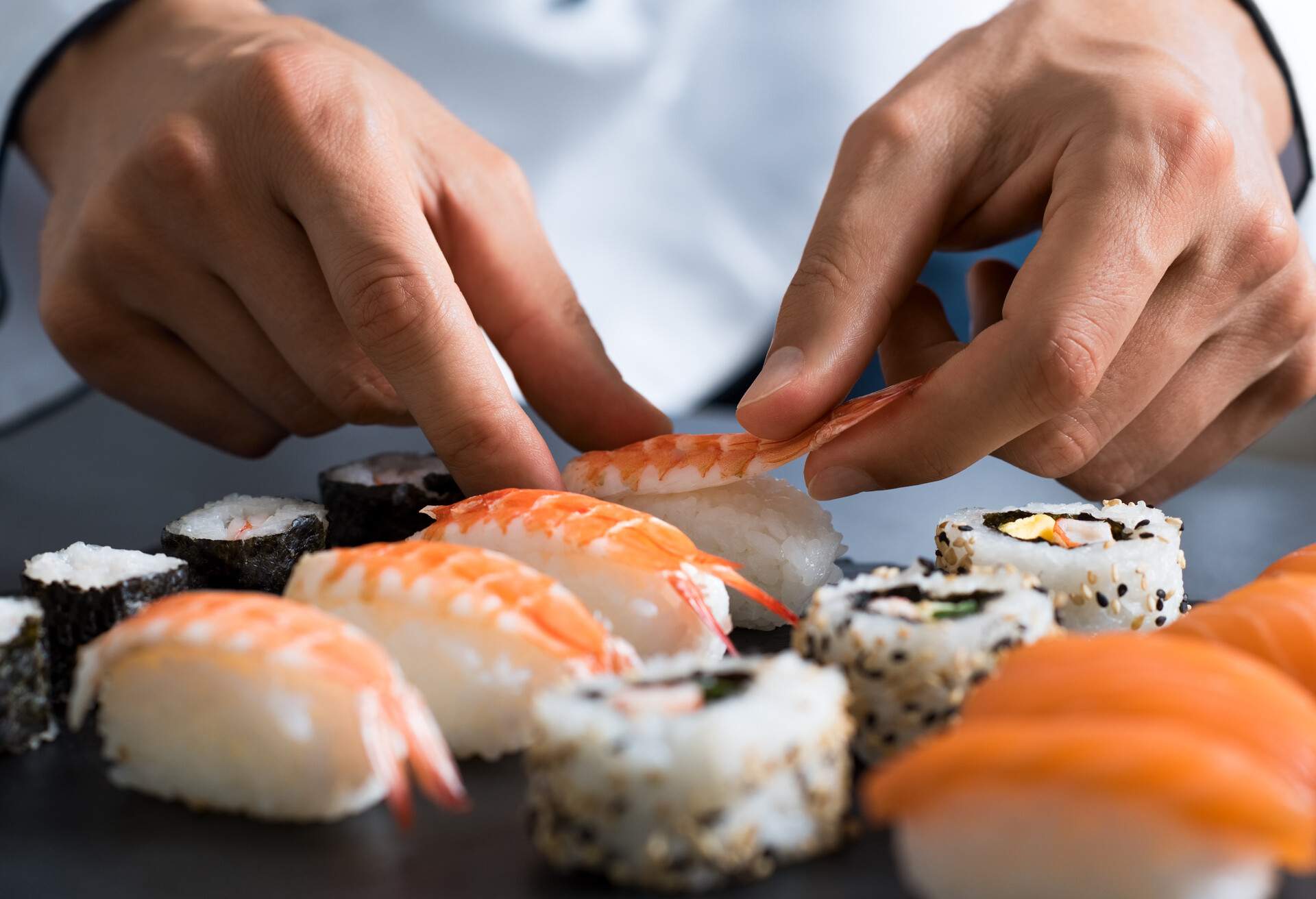 Closeup of chef hands preparing japanese food. Japanese chef making sushi at restaurant. Young chef serving traditional japanese sushi served on a black stone plate.