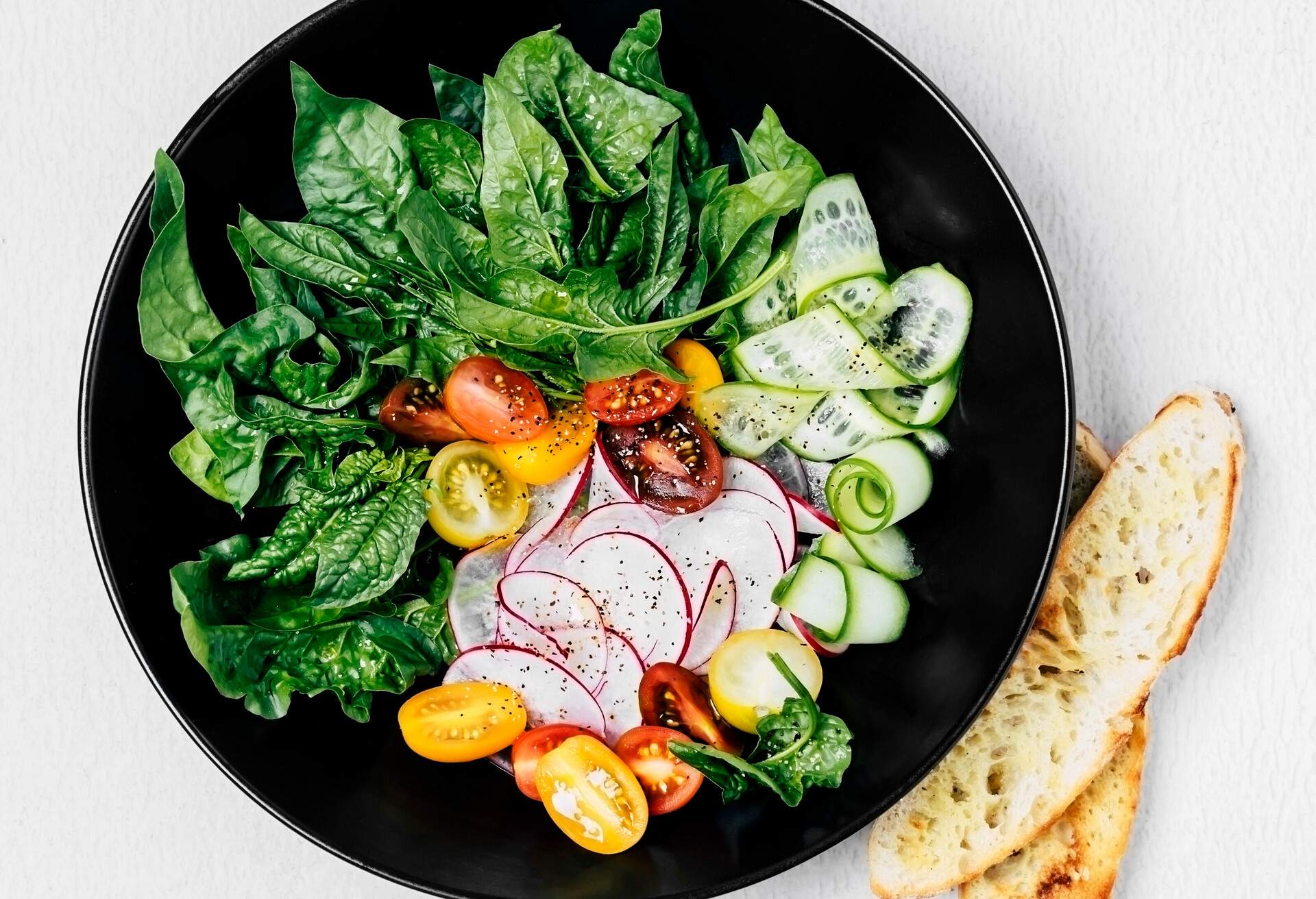 A bowl of fresh spring salad with a few slices of toasted bread on white background