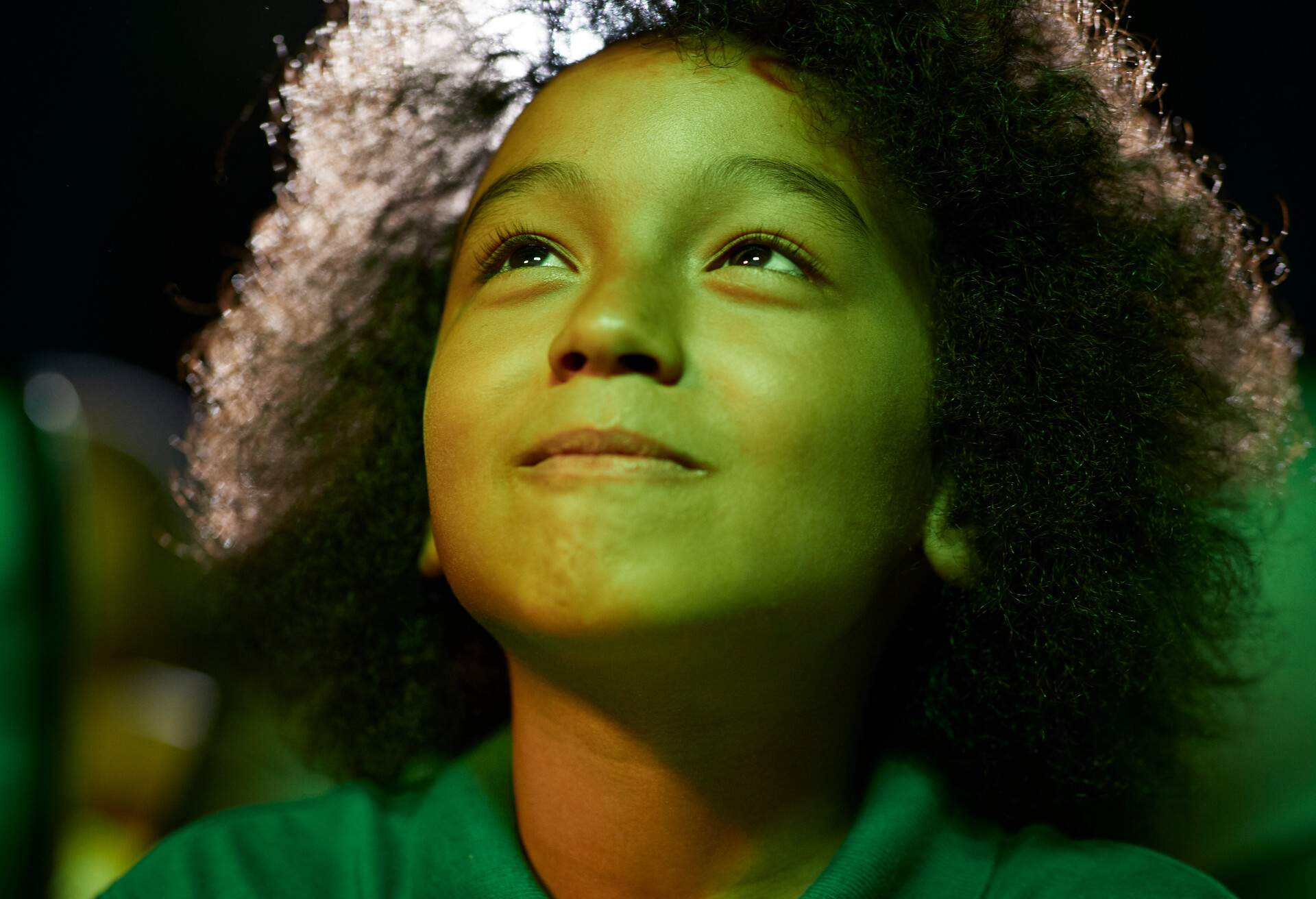 A curious boy with afro hair gazes upwards in wonder, surrounded by the dimly lit ambiance of a theater.