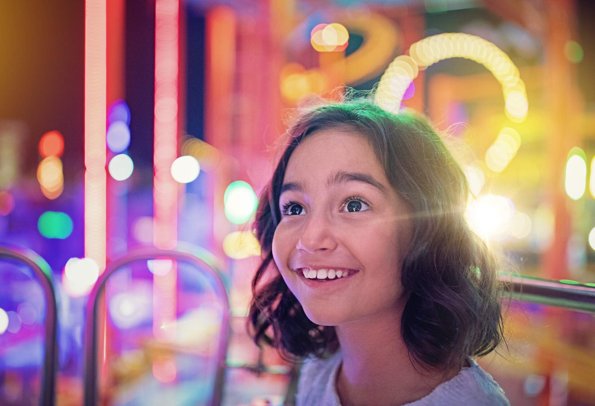A little girl beaming with delight as she looks around an amusement park.