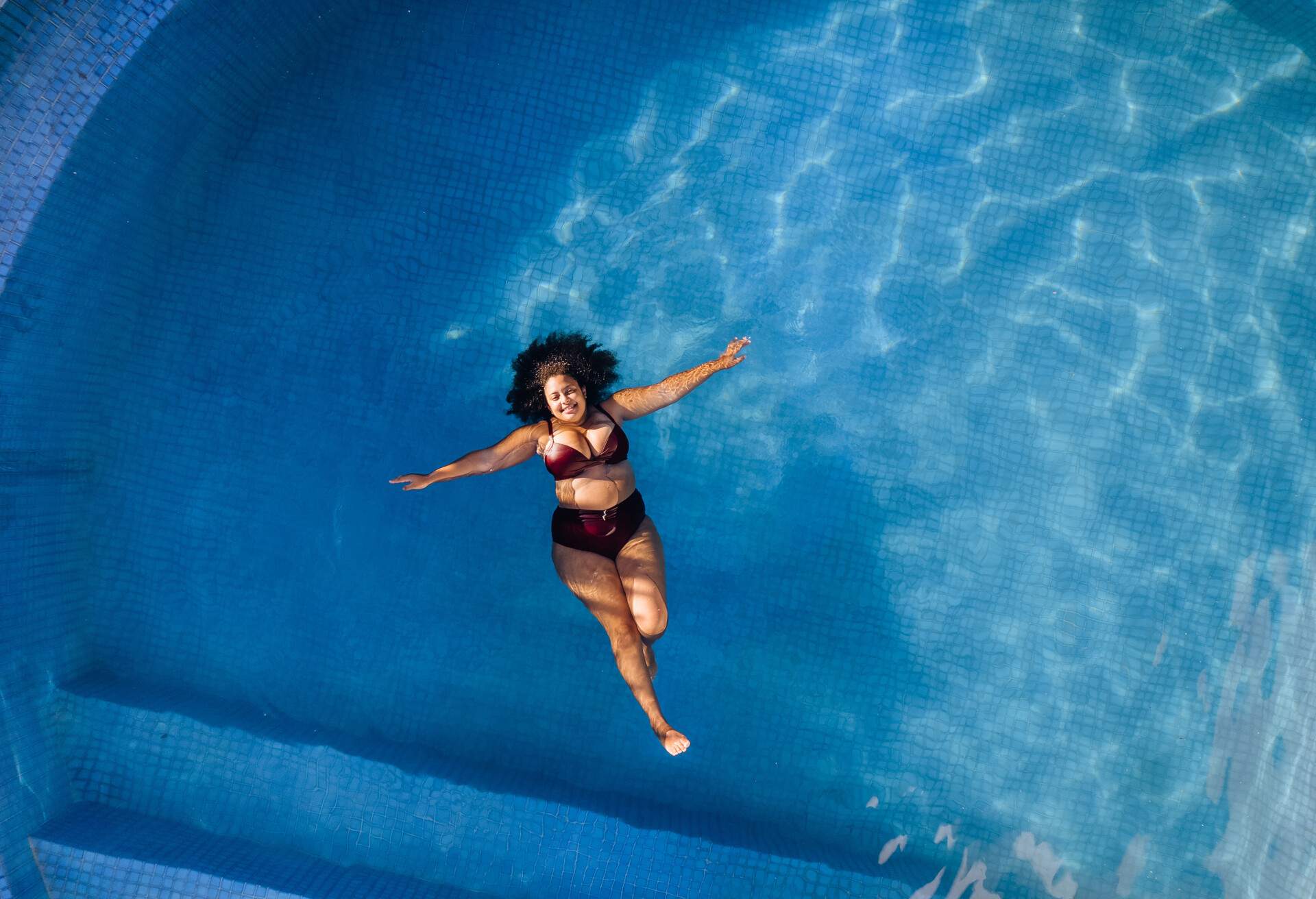 A woman in a bikini relaxes in a swimming pool, floating peacefully in the cool and refreshing water.
