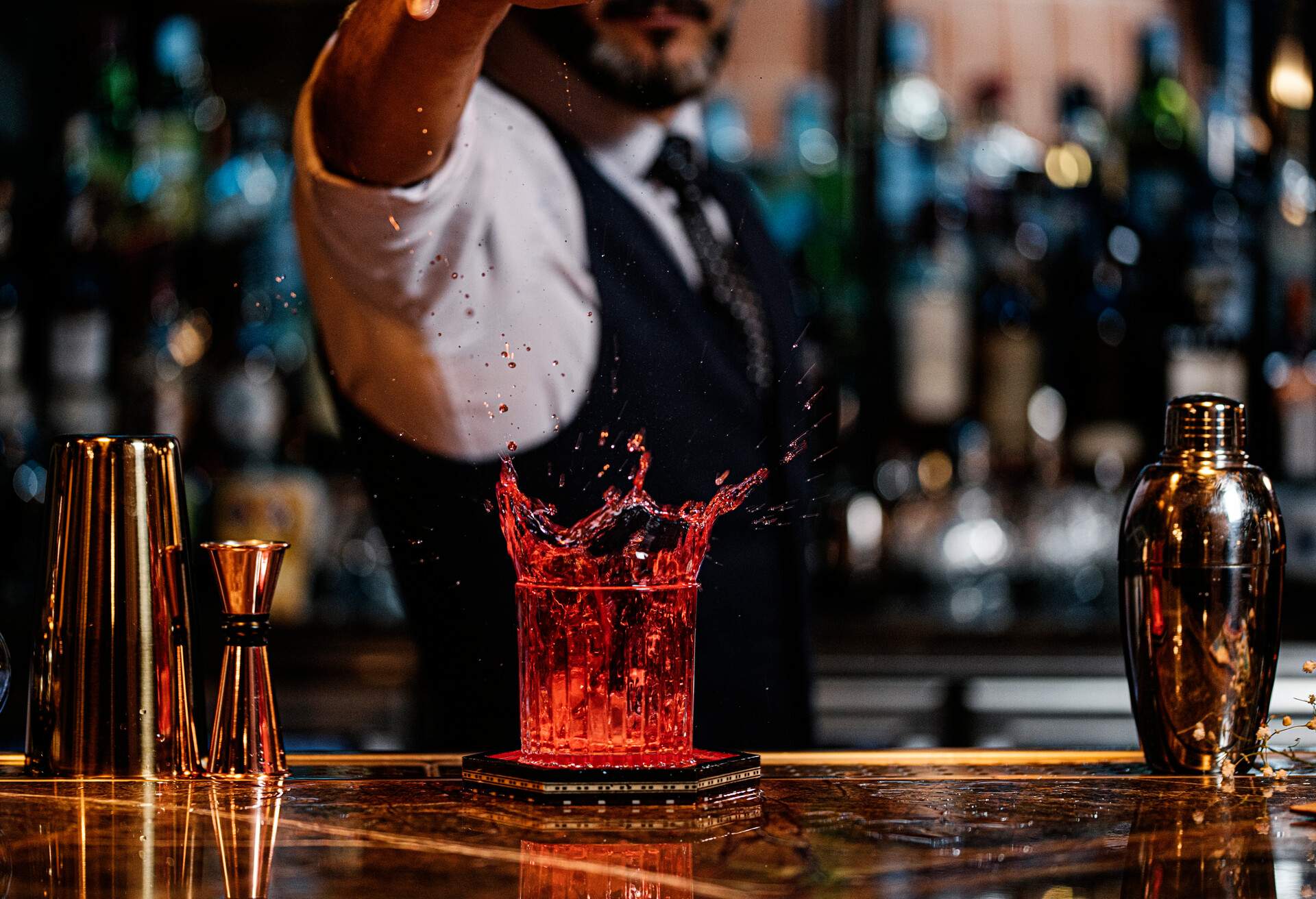 A male bartender pouring a red cocktail drink into a glass.