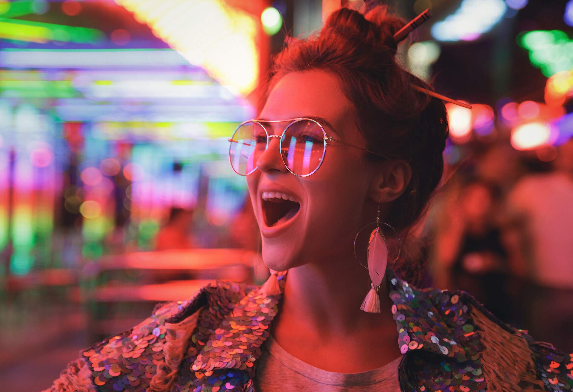 A portrait of a happy woman in a sparkling sequence jacket on the street with colourful lights.
