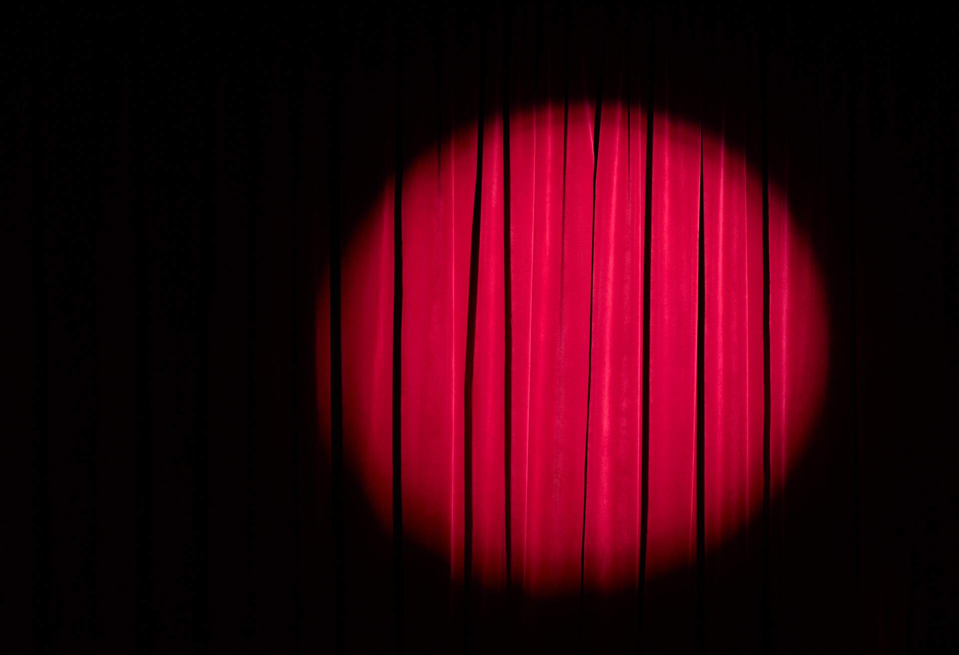 A circle spotlight shining on a red curtain.