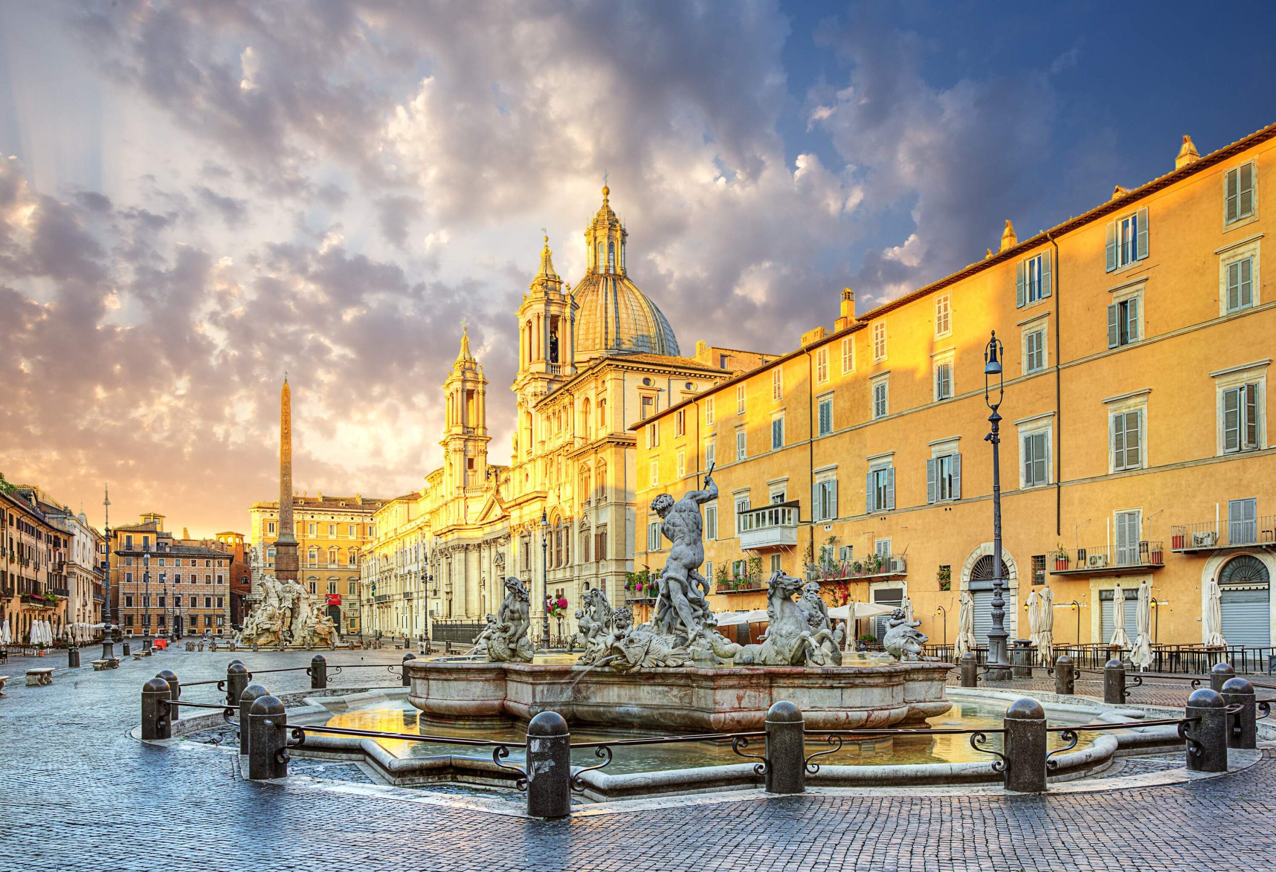 A bustling town square surrounded by buildings with two towers, featuring the stunning Fontana del Nettuno in the centre.