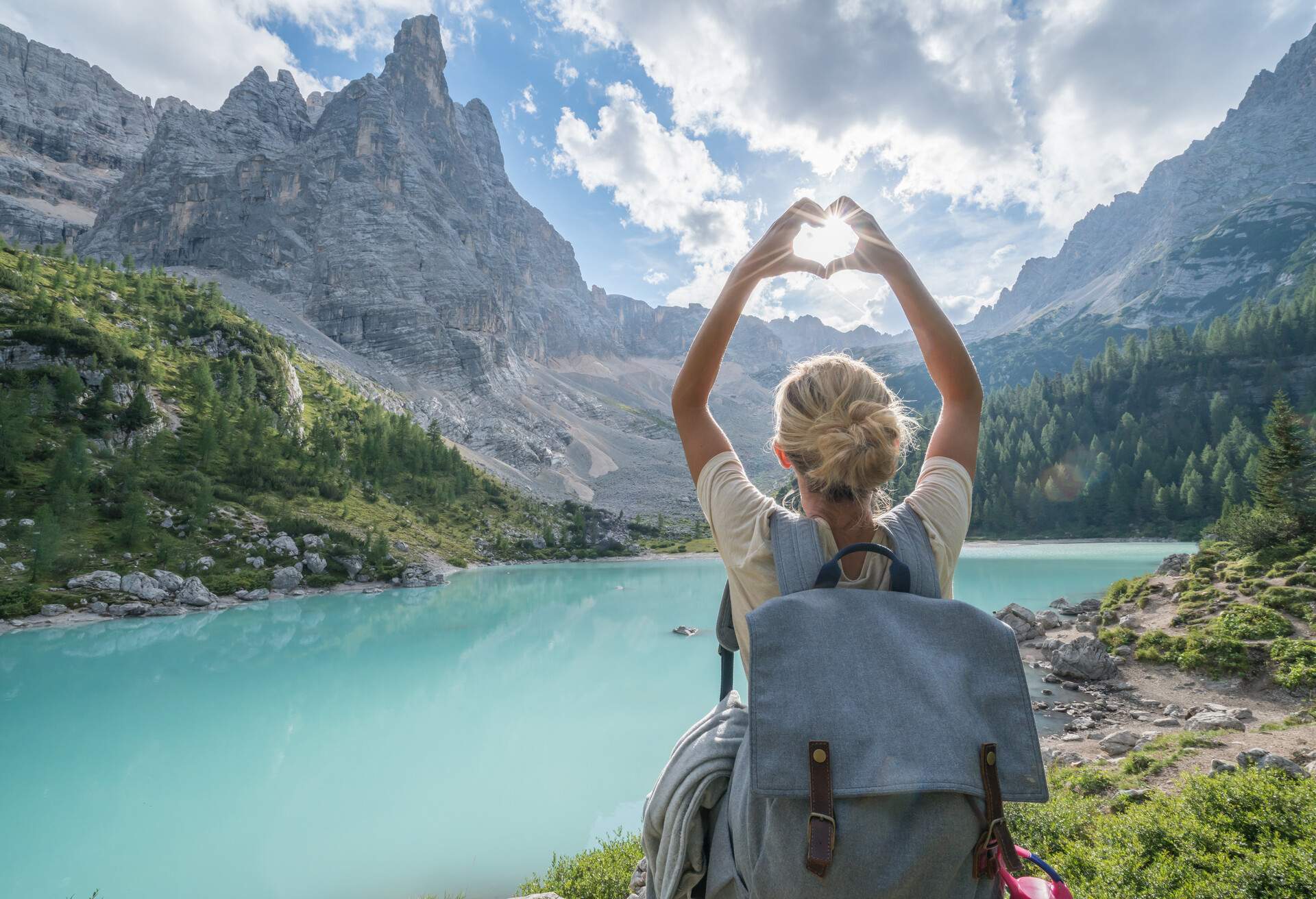 Young woman making heart shape finger frame on Alpine lake in Alto Adige region, Italy.