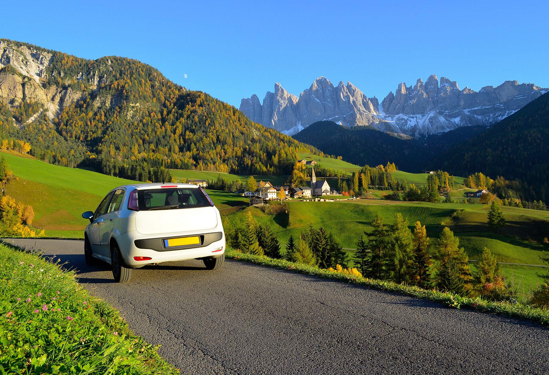 Road trip in a white car in autumn through the Funes valley in Dolomites area in South Tyrol, Italy..