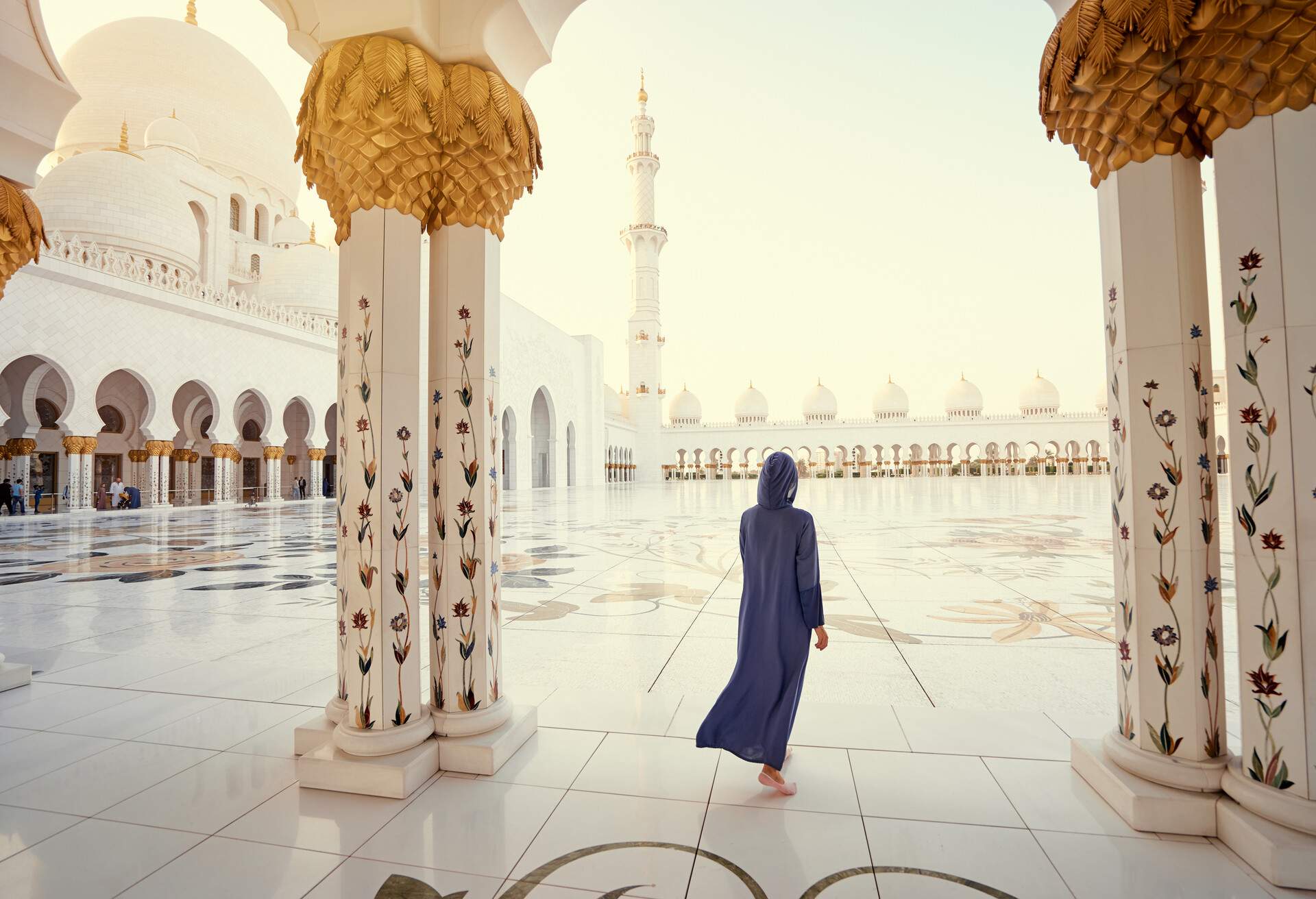 A woman in a blue robe walking towards the courtyard of the Sheikh Zayed Grand Mosque.