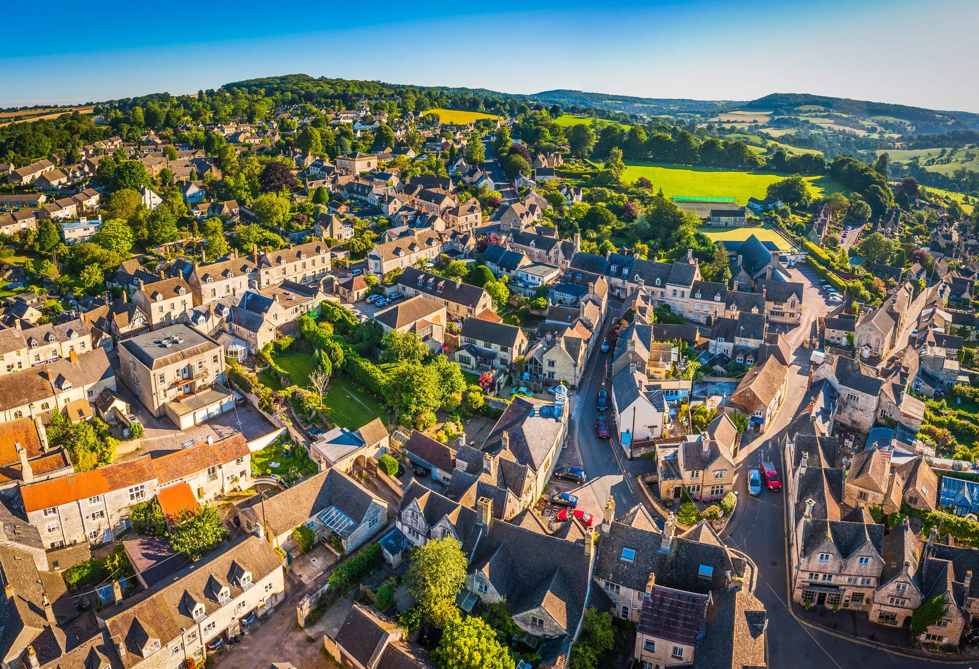 Aerial view over the iconic Cotswold village of Painswick, with its honey coloured limestone cottages deep in the bucolic countryside of Gloucestershire, UK, framed by vibrant green patchwork fields and clear blue summer skies. ProPhoto RGB profile for maximum color fidelity and gamut.