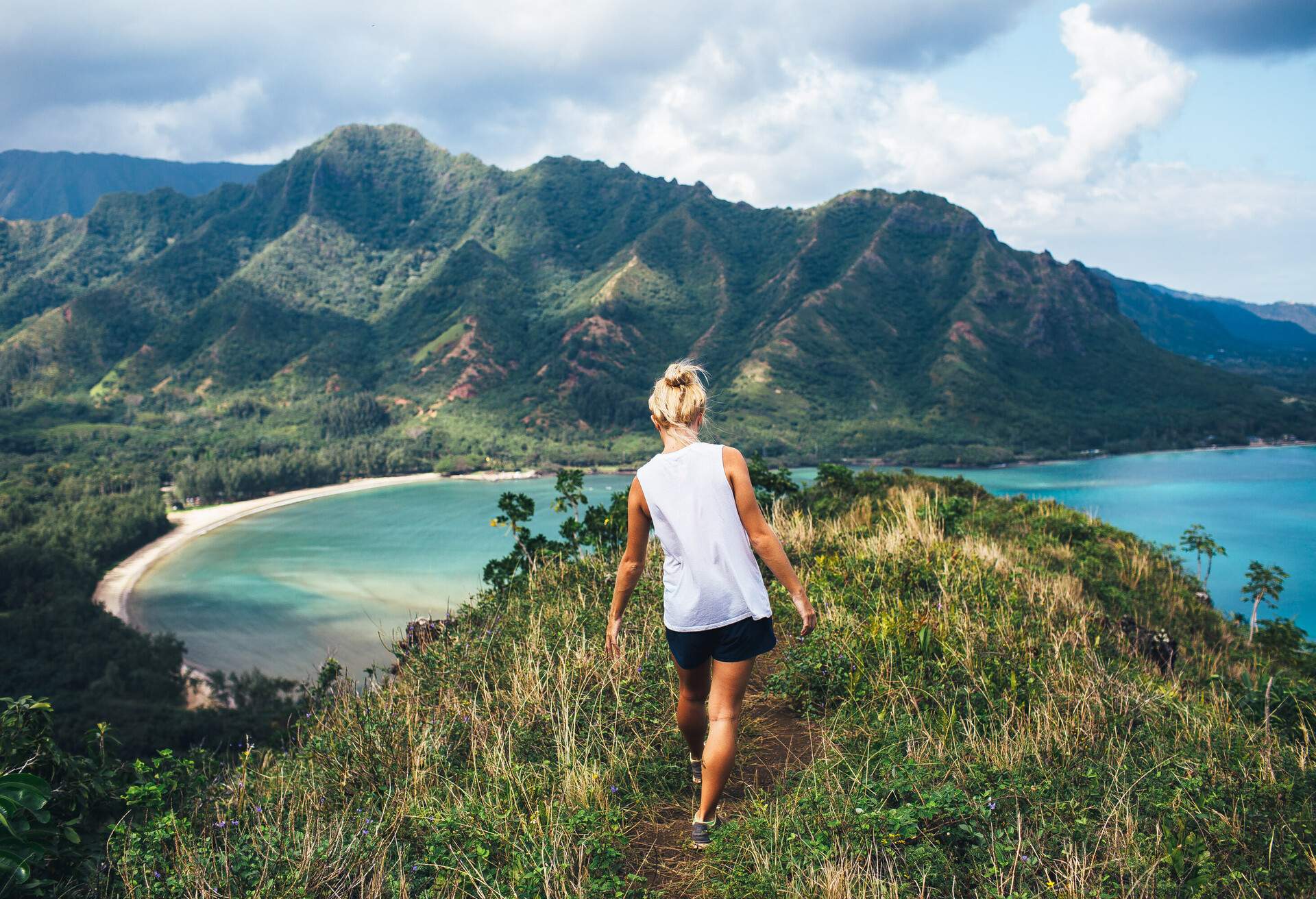 A woman walking toward the hilltop overlooking a beach with milky blue water.