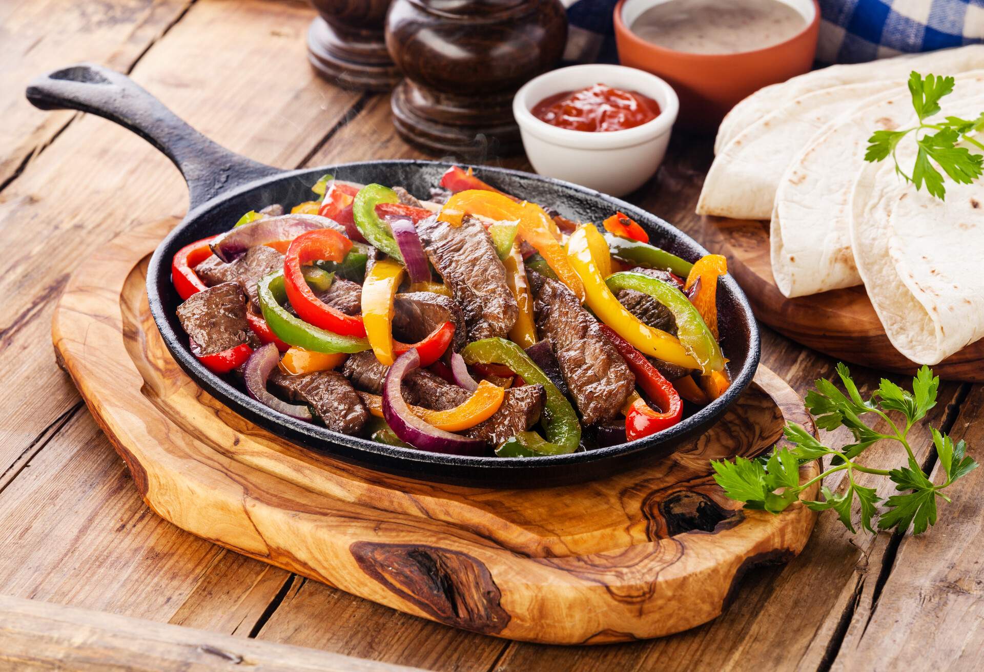 Beef Fajitas with colorful bell peppers in pan and tortilla bread and sauces