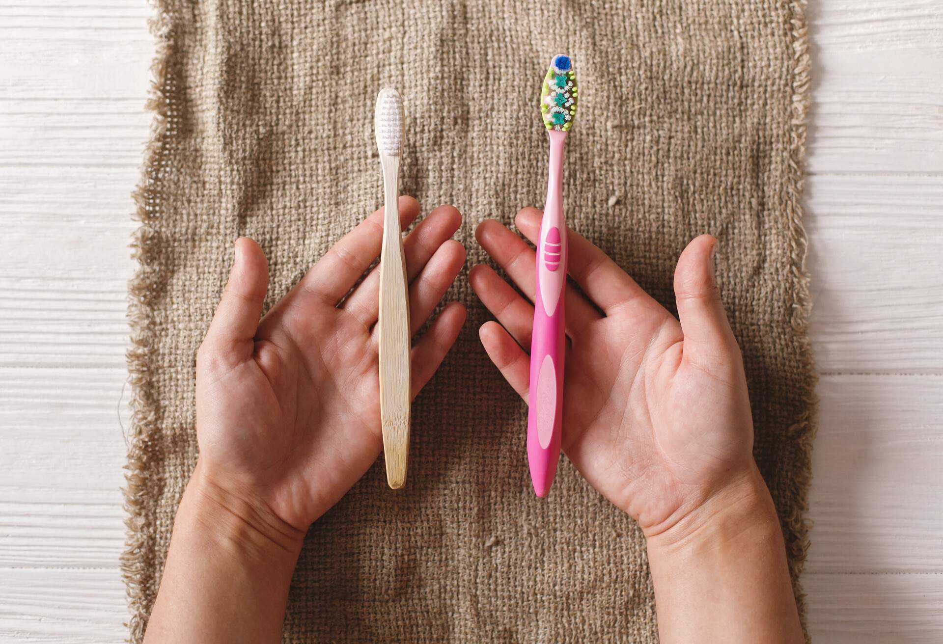 hand holding eco natural bamboo toothbrush and in other hand plastic toothbrush, flat lay on rustic background. sustainable lifestyle concept. zero waste. choice plastic free items; Shutterstock ID 1170203749; Purpose: Plastic free travel tips; Brand (KAYAK, Momondo, Any): momondo