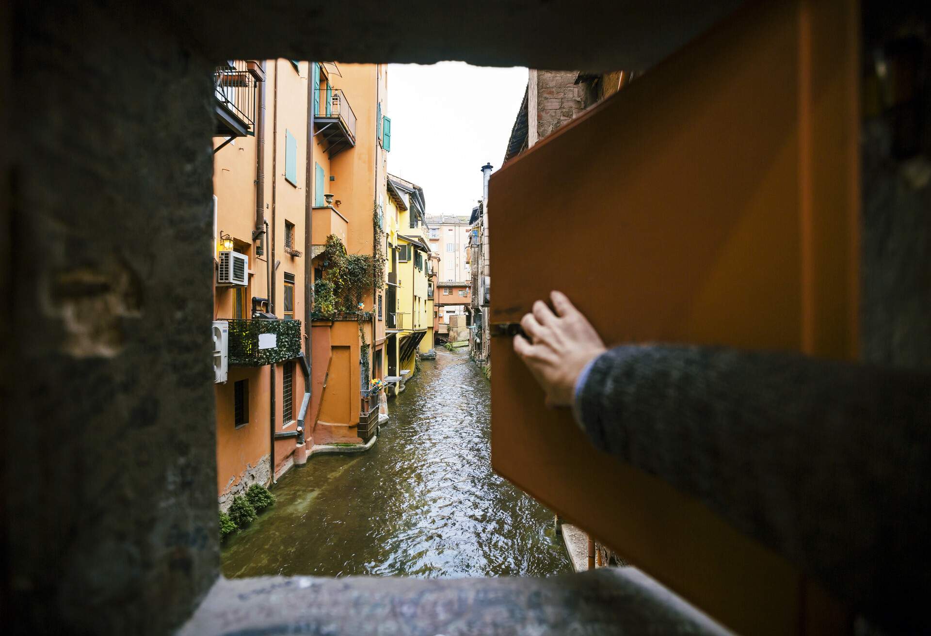 Hand opening Bologna's window (finestrella) on the canal, italy