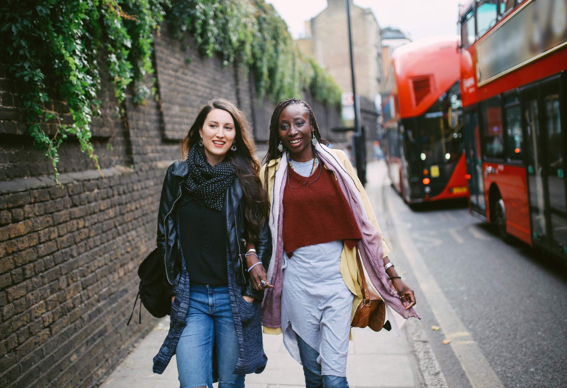 two girlfriends walking on London street on an autumn day, red buses on background