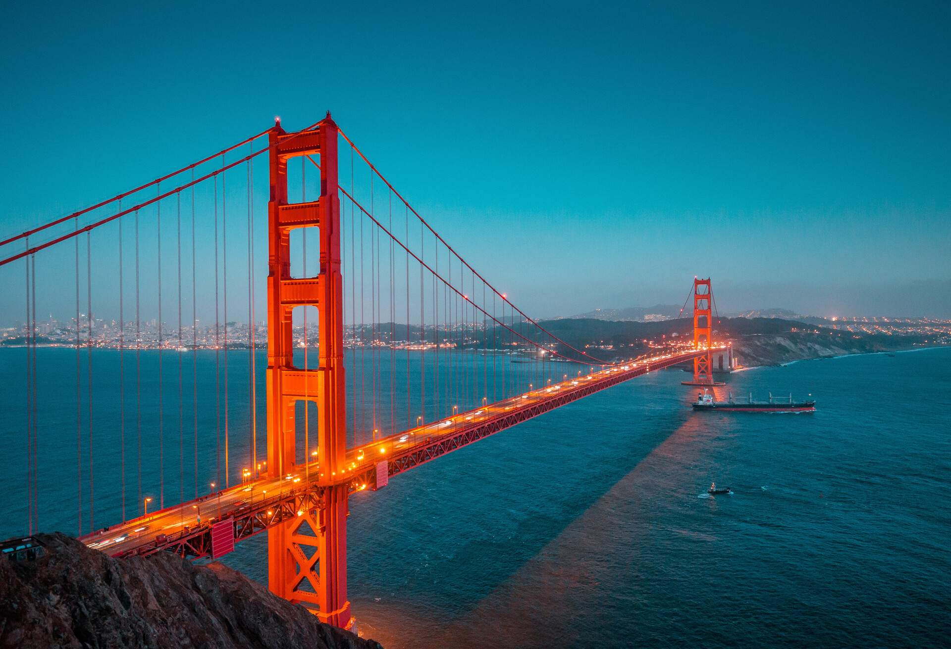 Classic panoramic view of famous Golden Gate with cargo freight ship in beautiful post sunset twilight during blue hour at dusk in summer, San Francisco, California, USA