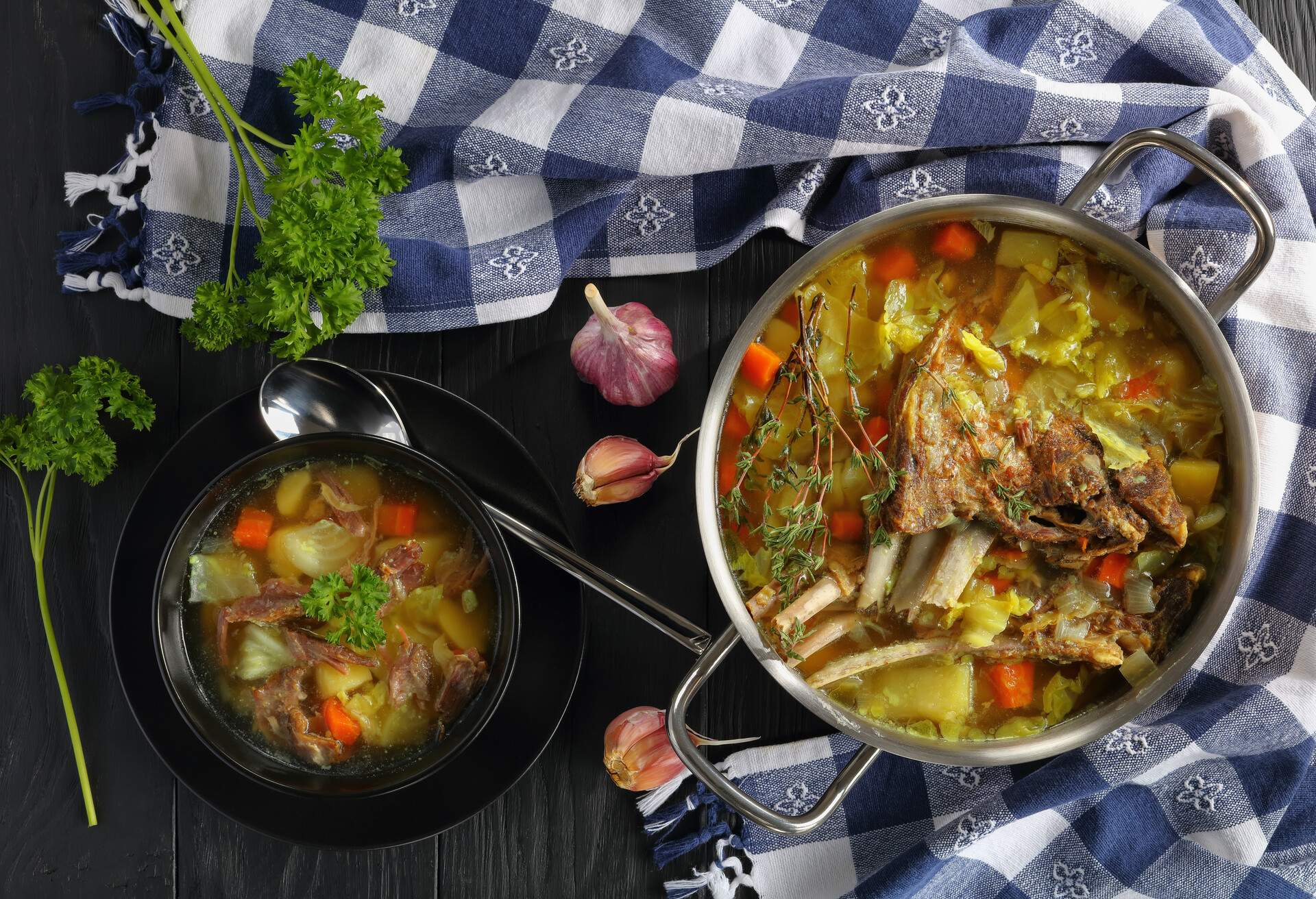 close-up of delicious Icelandic Lamb Soup with vegetables and spices or kjotsupa in a stainless steel casserole pan  and in bowl on wooden table with kitchen towel, traditional recipe, view from above