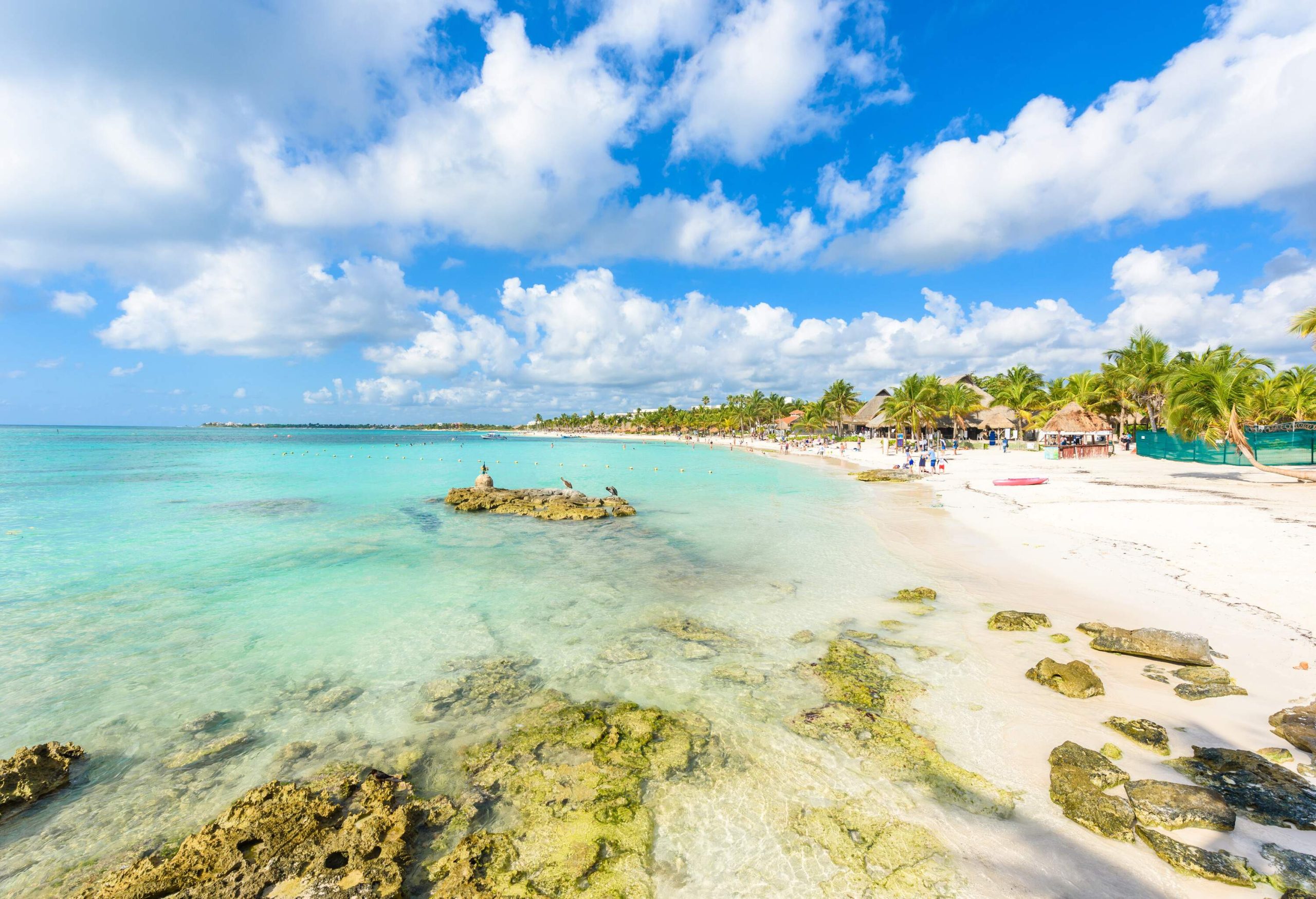 A picturesque long beach with crystal clear turquoise water and fine white sands bordered by a rocky shore.