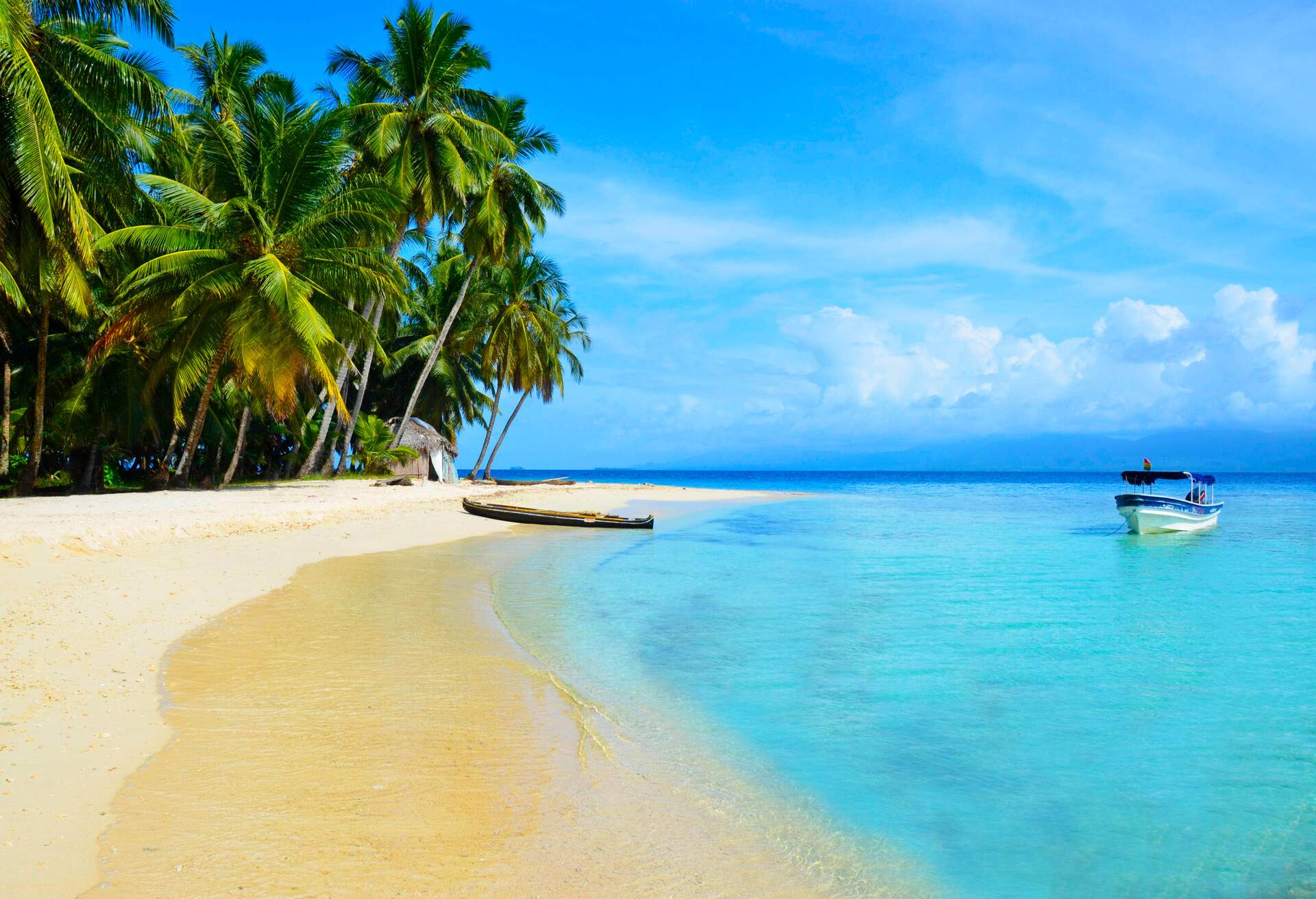 Sunny beach with palm tress and two boats in San Blas Island Kuna Yala in Panama