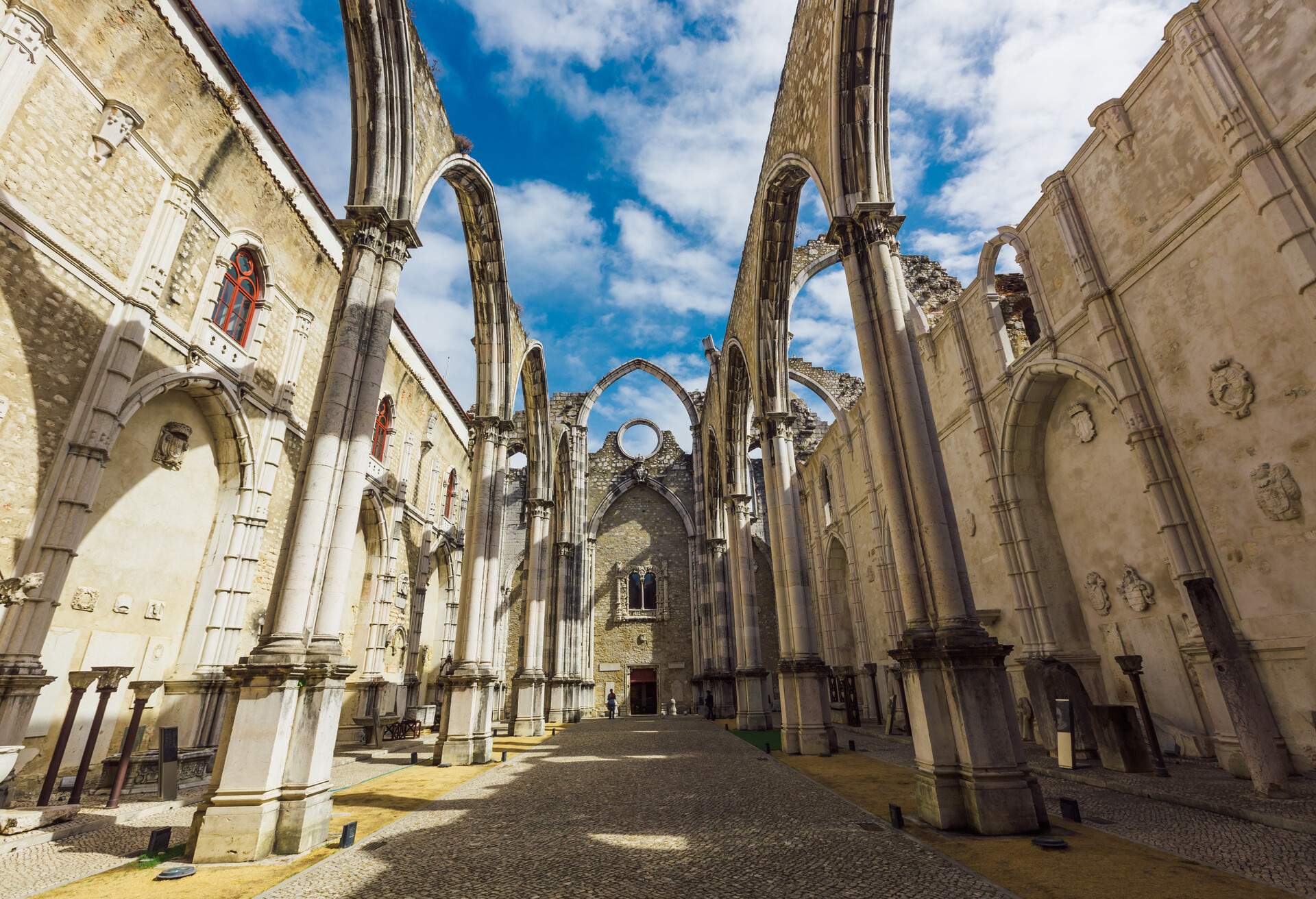 A cobbled pathway surrounded by arcades leading to the entryway of an antique church.