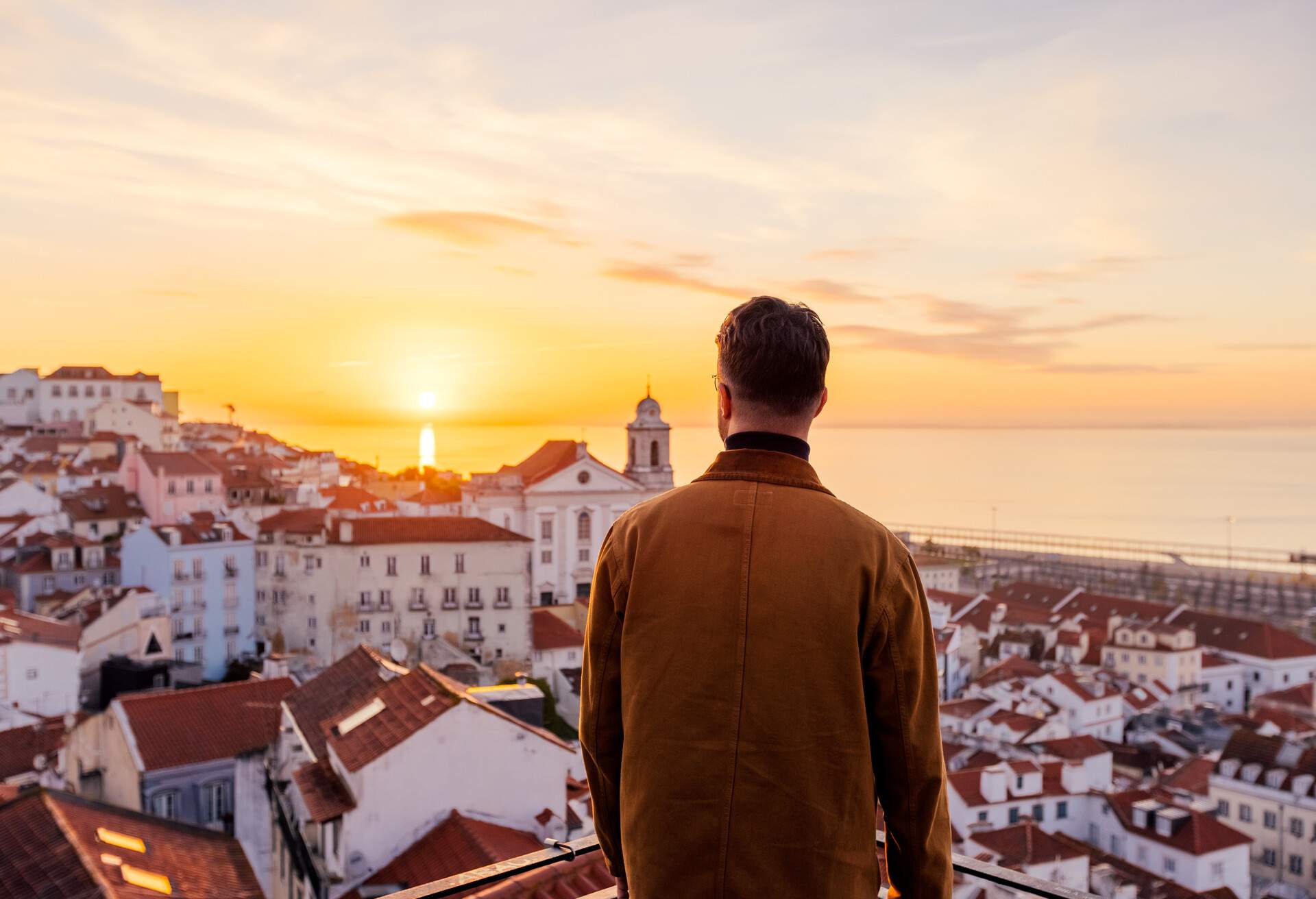 Rear view of a man looking at Lisbon skyline at sunrise, Portugal