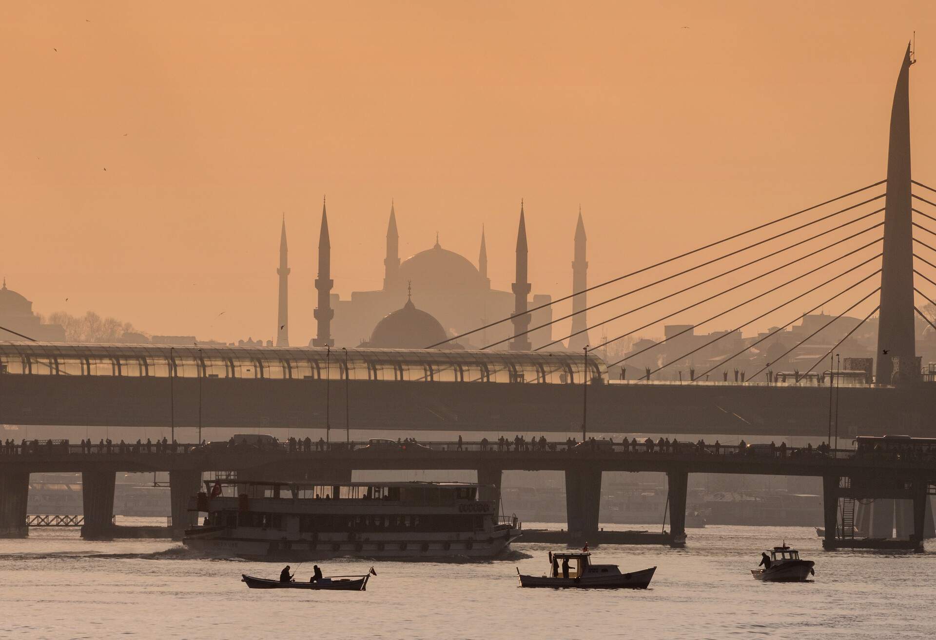 Distant view of The silhouetted New Mosque,The Hagia Sophia, The Metro Bridge and The Unkapani Bridge( spanning the Golden Horn)  with small fishing boats(sandal), seen from the Golden Horn ferry in the morning, in Istanbul, Turkey.