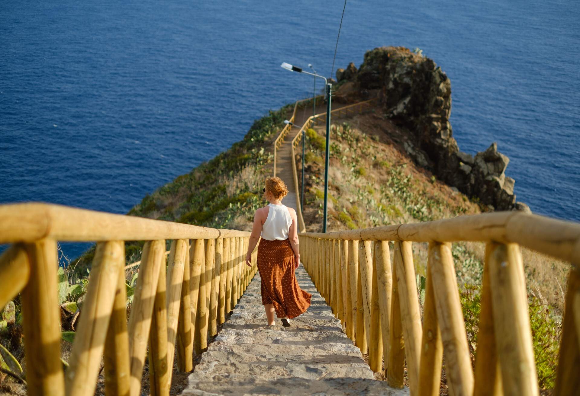 A person gracefully descends a stairway leading to a viewpoint overlooking the sea.