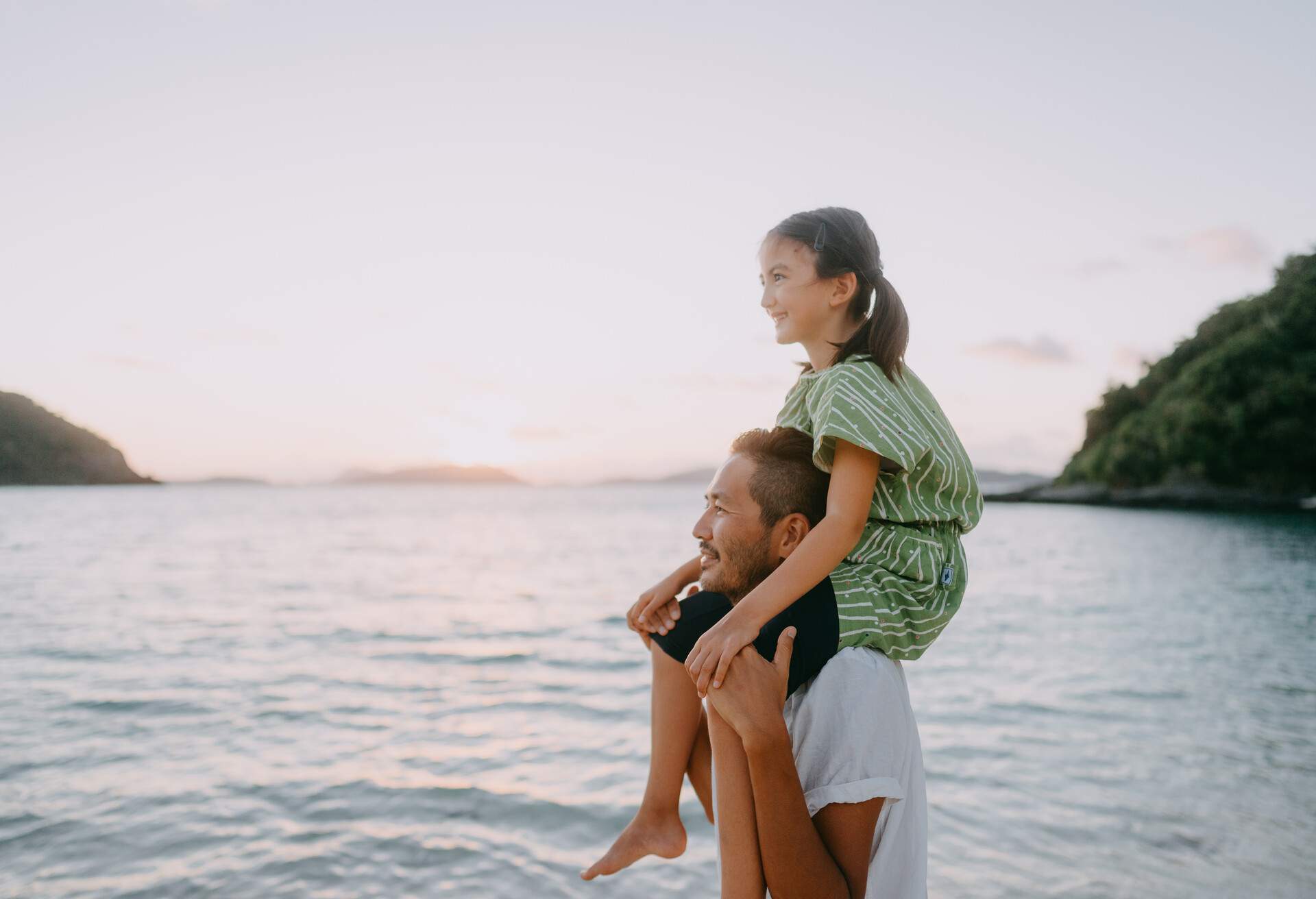 Japanese father carrying his young daughter on shoulders on beach at sunset, Tokashiki Island of Kerama Shoto National Park, Okinawa, Japan