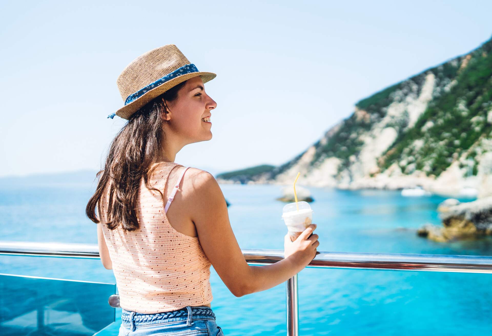 Young caucasian woman on a boat ride at sea enjoying at view and milkshake.