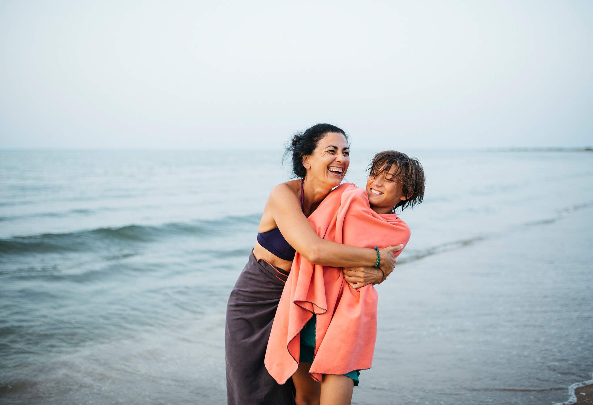 Portrait of a smiling mature woman and her twelve years old boy, embracing on the beach during sunset