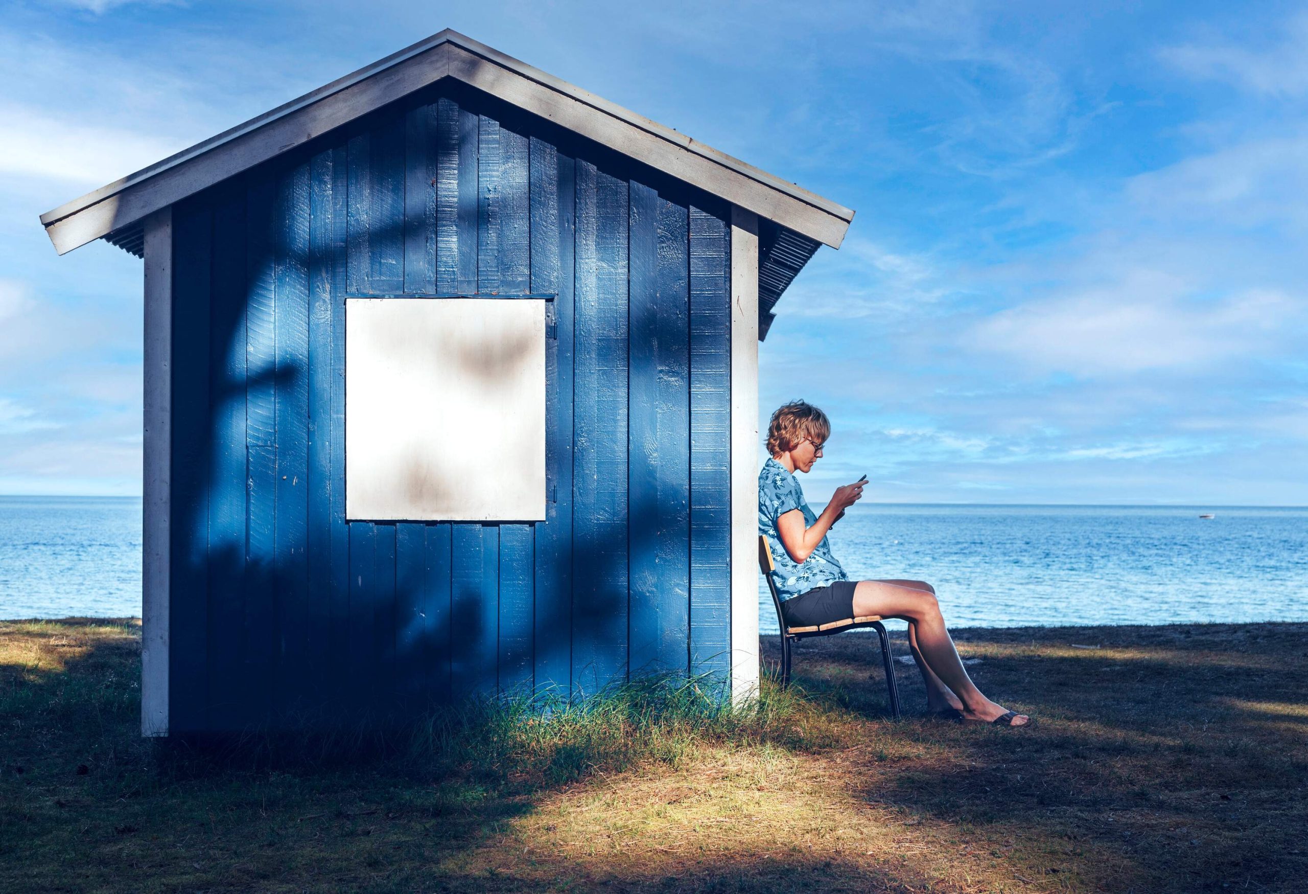 Woman sitting by a traditional blue wooden hut by the sea on a summer day