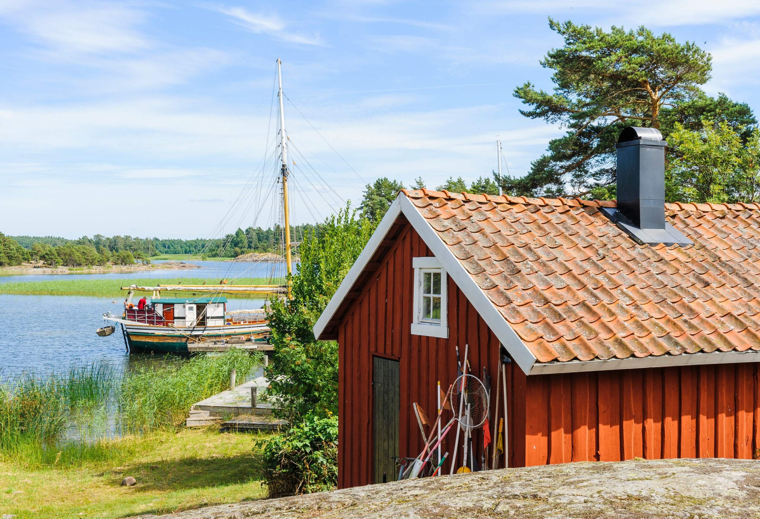 A red shack by a lake with a fishing boat docked nearby.