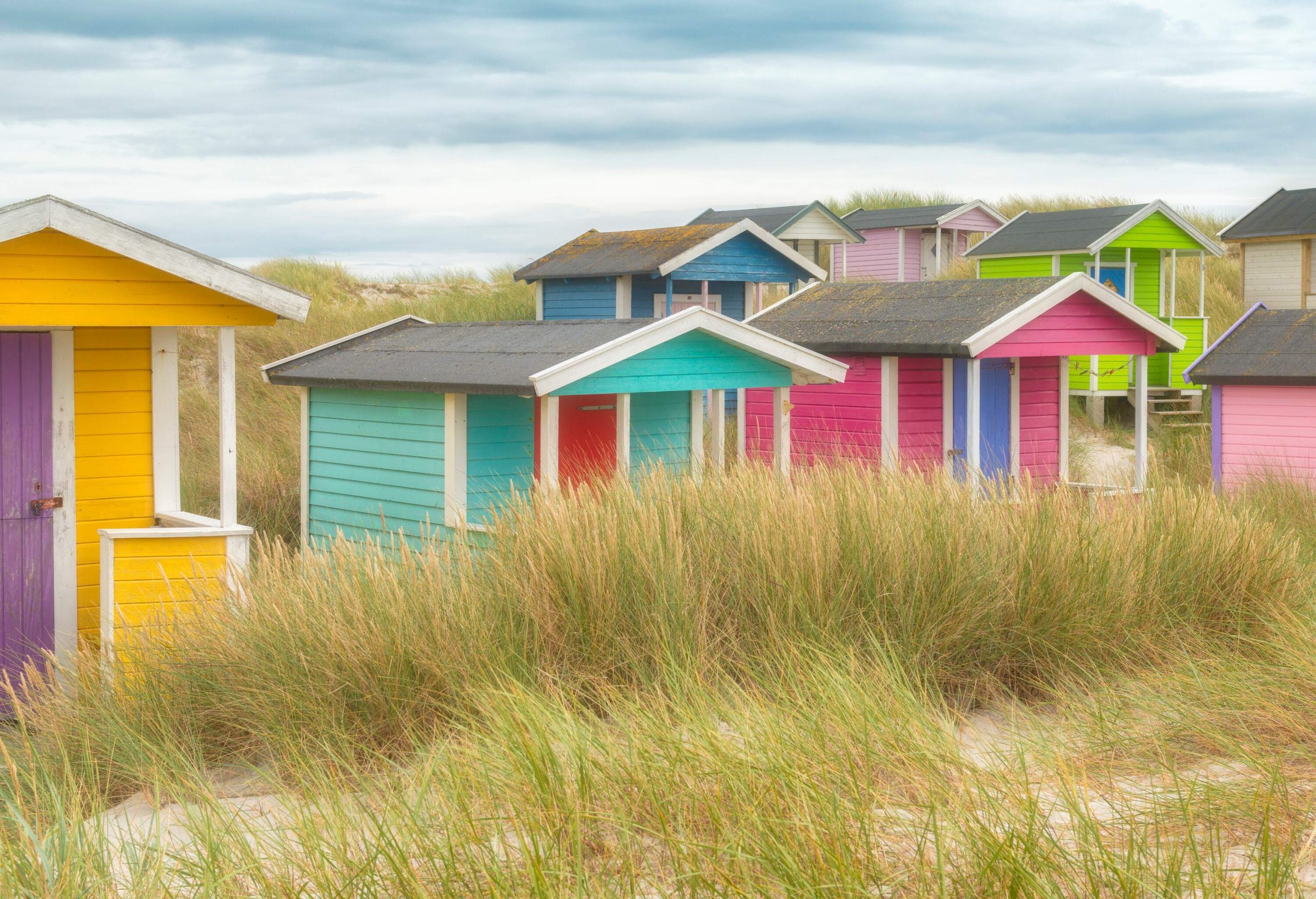 Brightly coloured wooden cabins scattered across a grassy beach.
