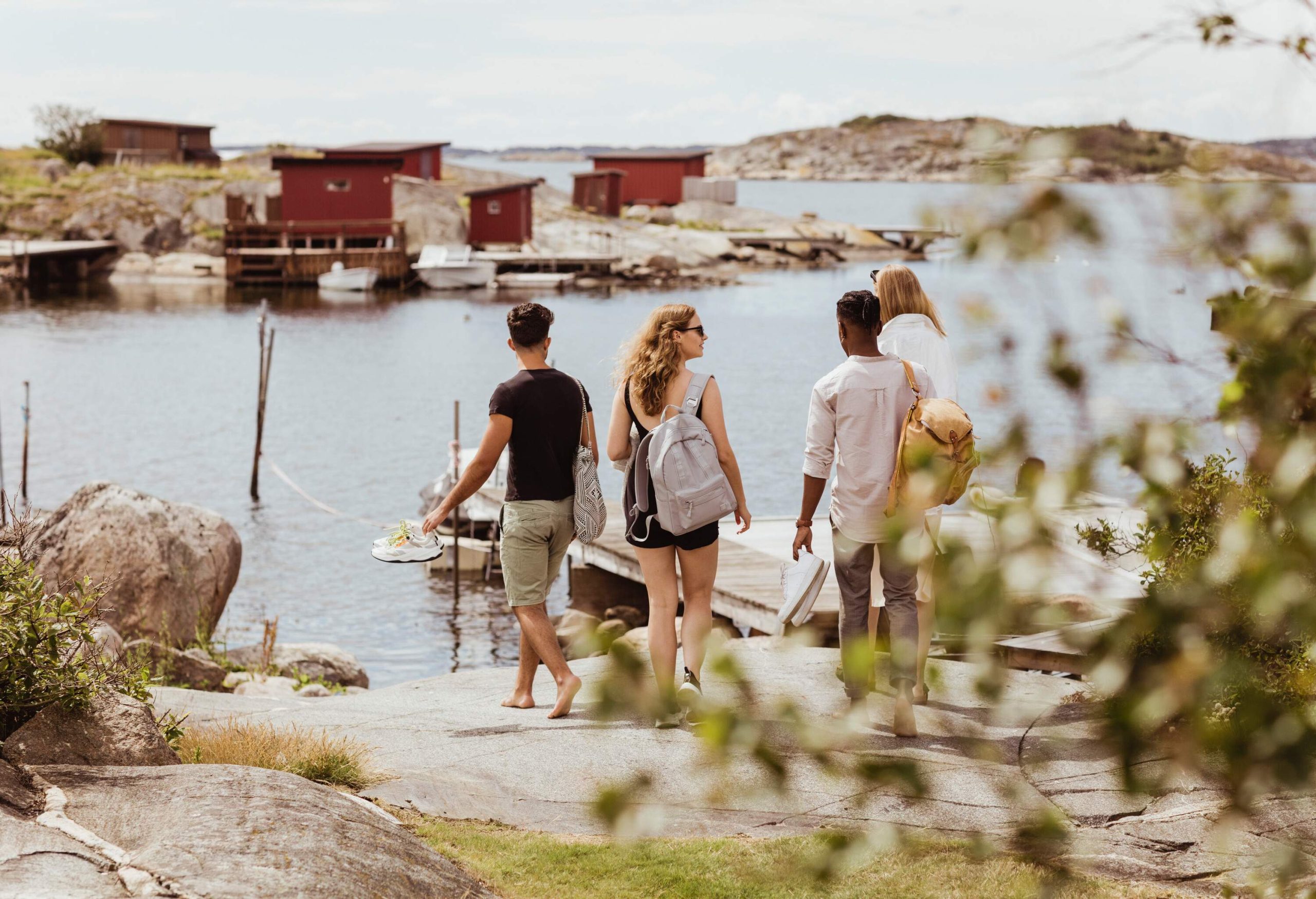 Four friends headed toward a wooden dock with a moored boat next to a small island with small maroon cottages.