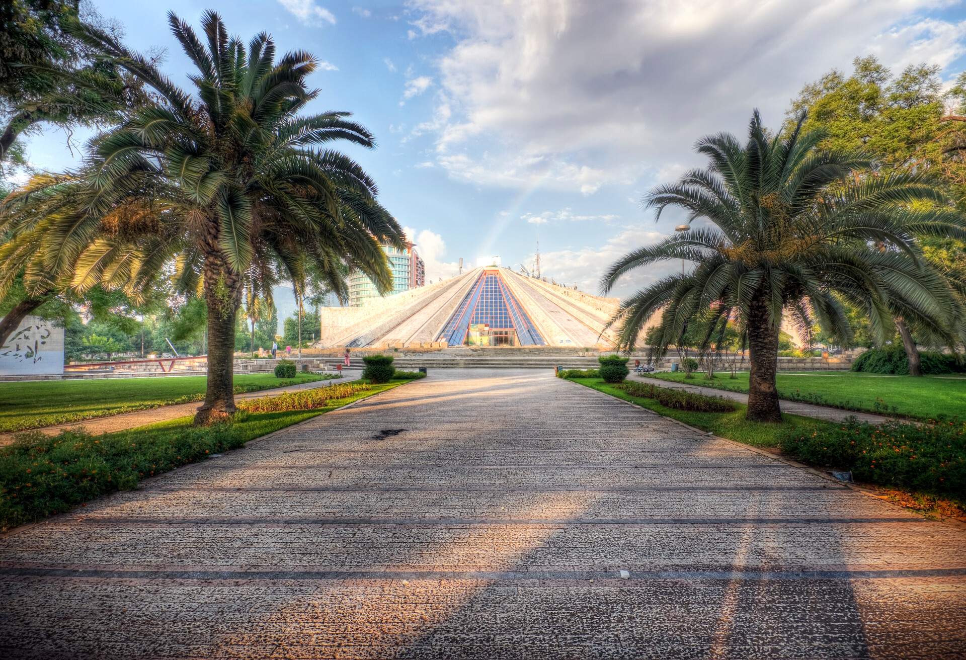 Tirana Albania: This national symbol was erected in 1985 by the daughter of the former communist dictator Enver Hoxha, with intentions of building a museum honoring the life of her father. Today the building awaits renovation and a new function. A rainbow can be seen emerging from right behind the pyramid after a brief rain storm. Photo processed for high dynamic range.