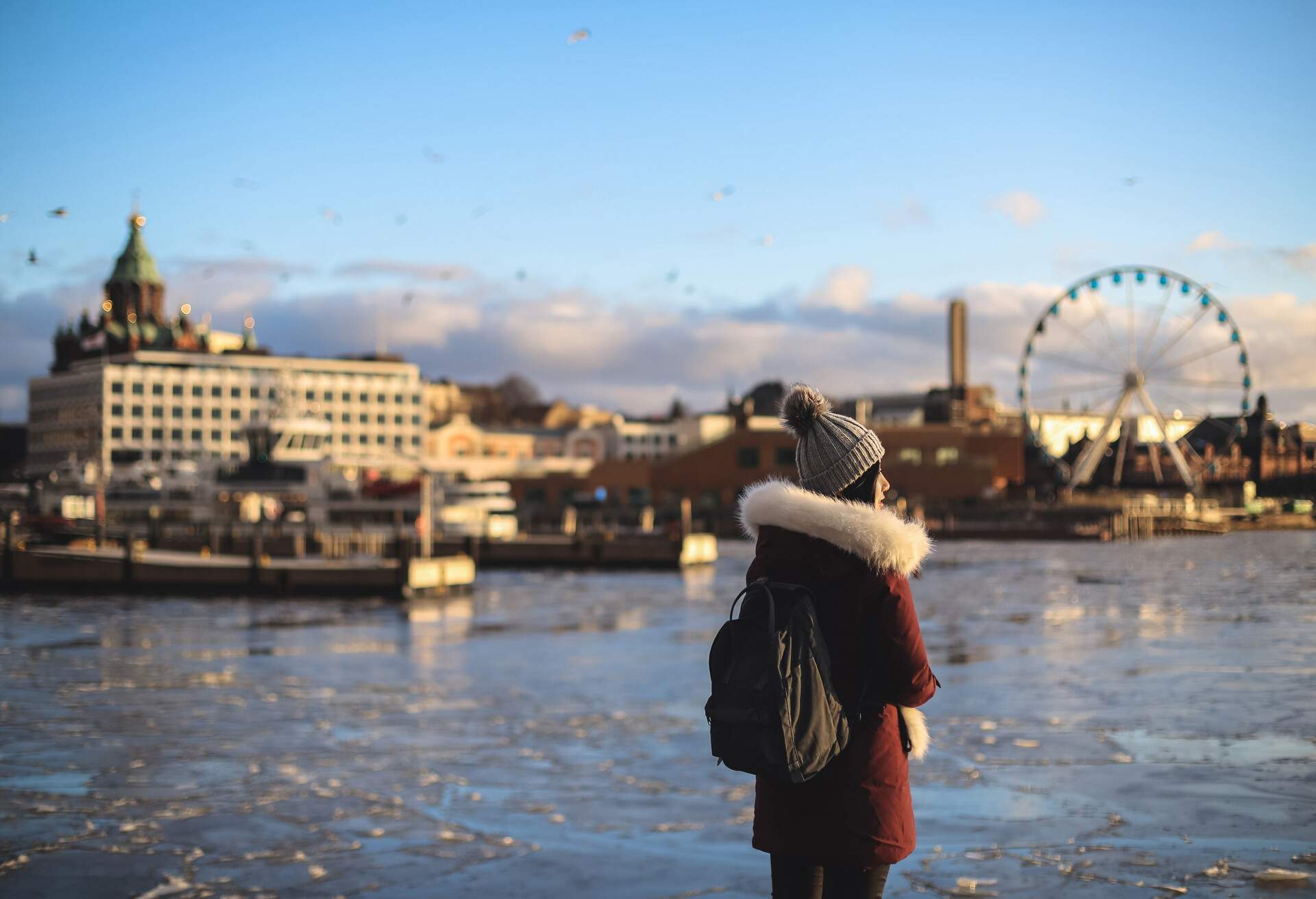 A woman in winter clothing and a blurred image of a cityscape with a big sky wheel in the background.