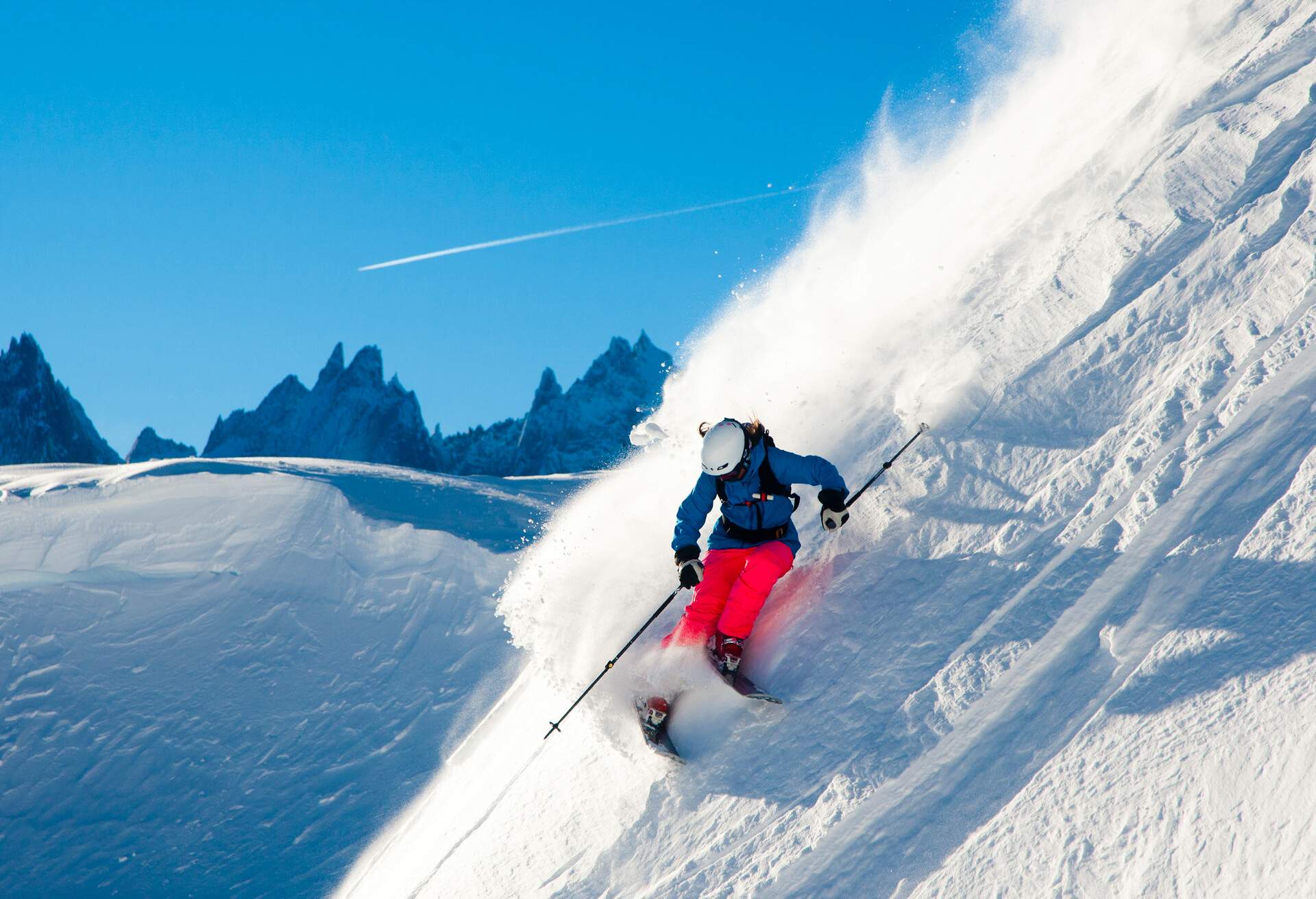 Skier descending down a steep hillside through fresh powder of snow.