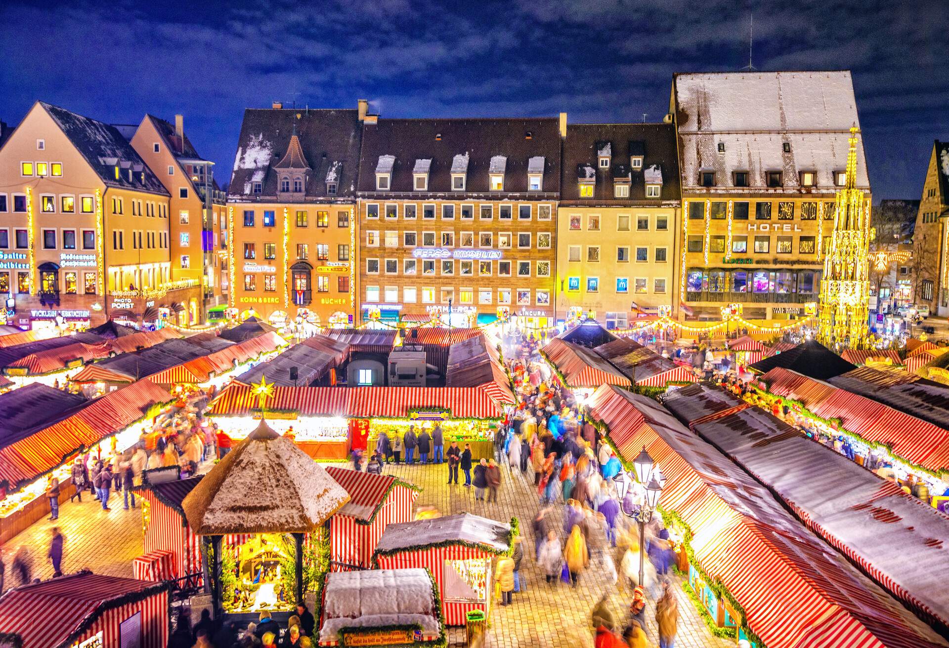 A busy Christmas market with rows of lit-up booths along the vibrant city structures.
