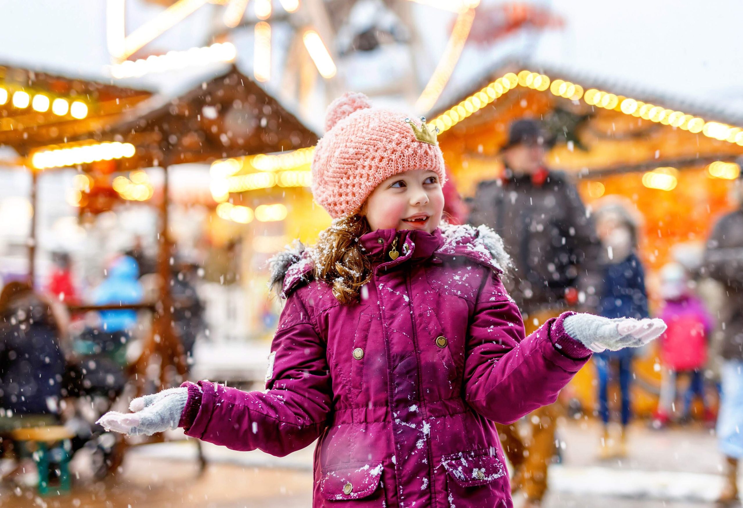 Little girl having fun on traditional German Christmas market during strong snowfall.. Happy child enjoying traditional family market in German. Laughing girl in colorful clothes.