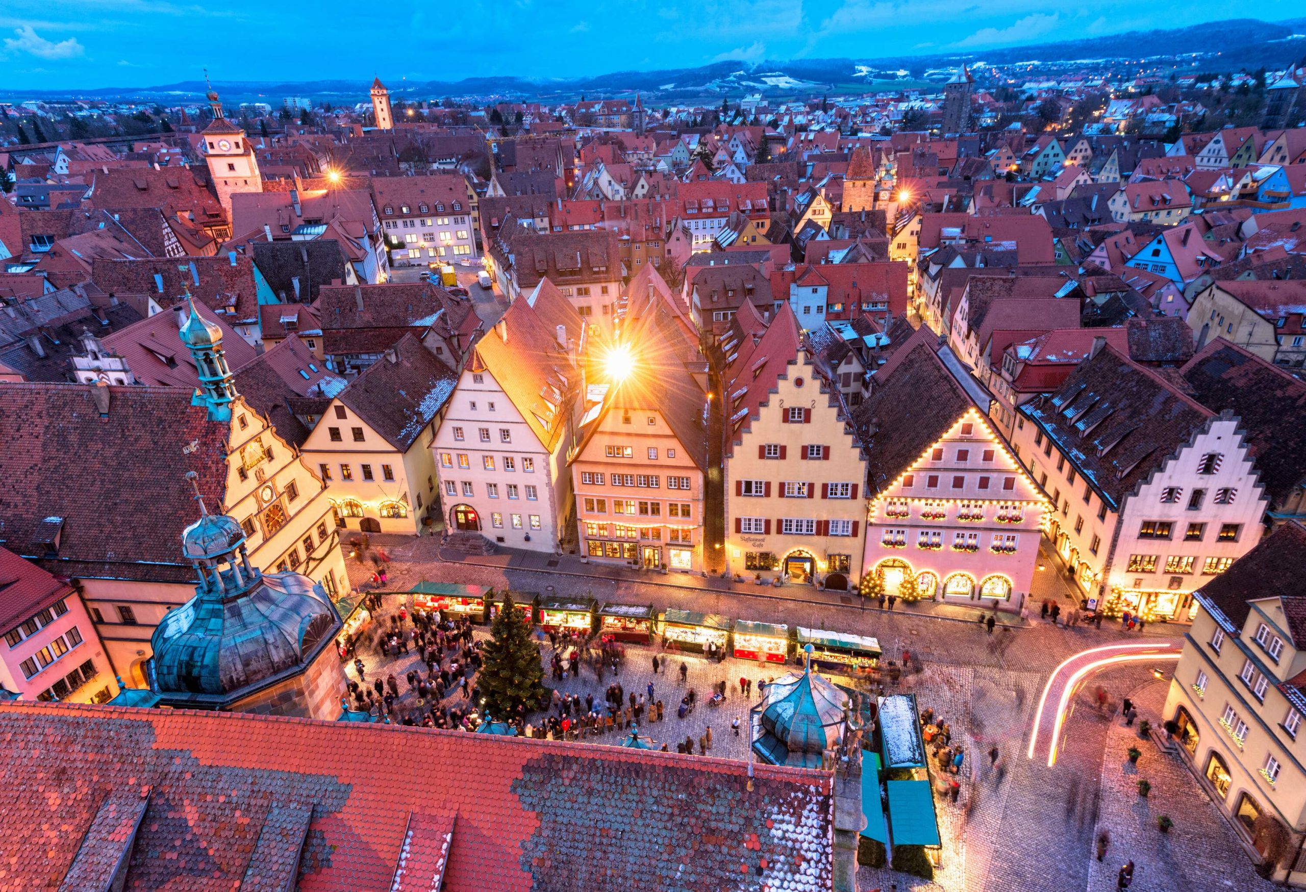 A city dominated by two towers protruding above the roofs of numerous houses alongside a Christmas market.