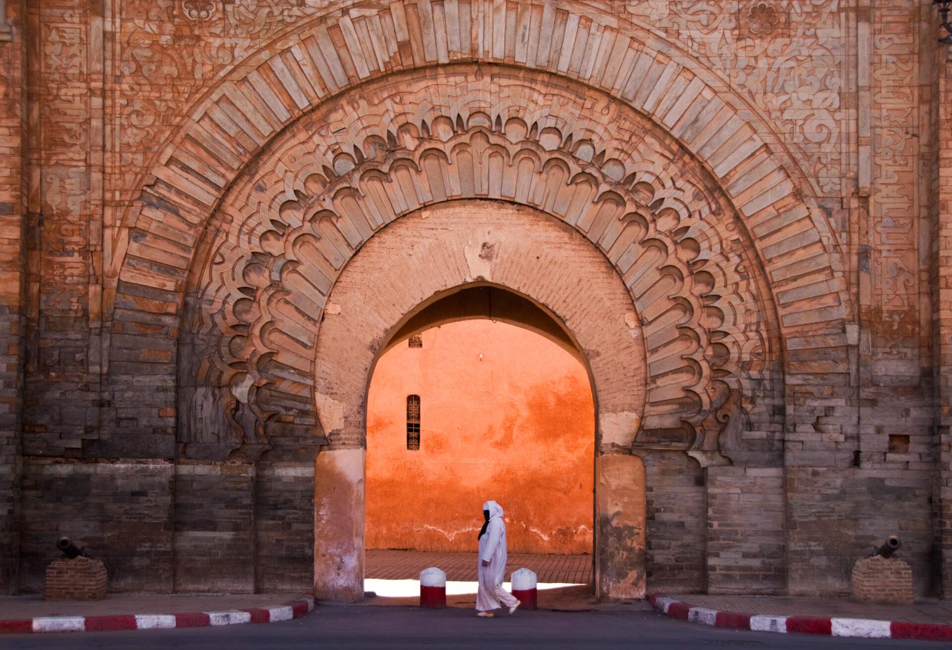 Woman in traditional arab clothing with veil passing by the Bab Anaou gate in Marrakech. The woman walks right in the middle of an orange gate 