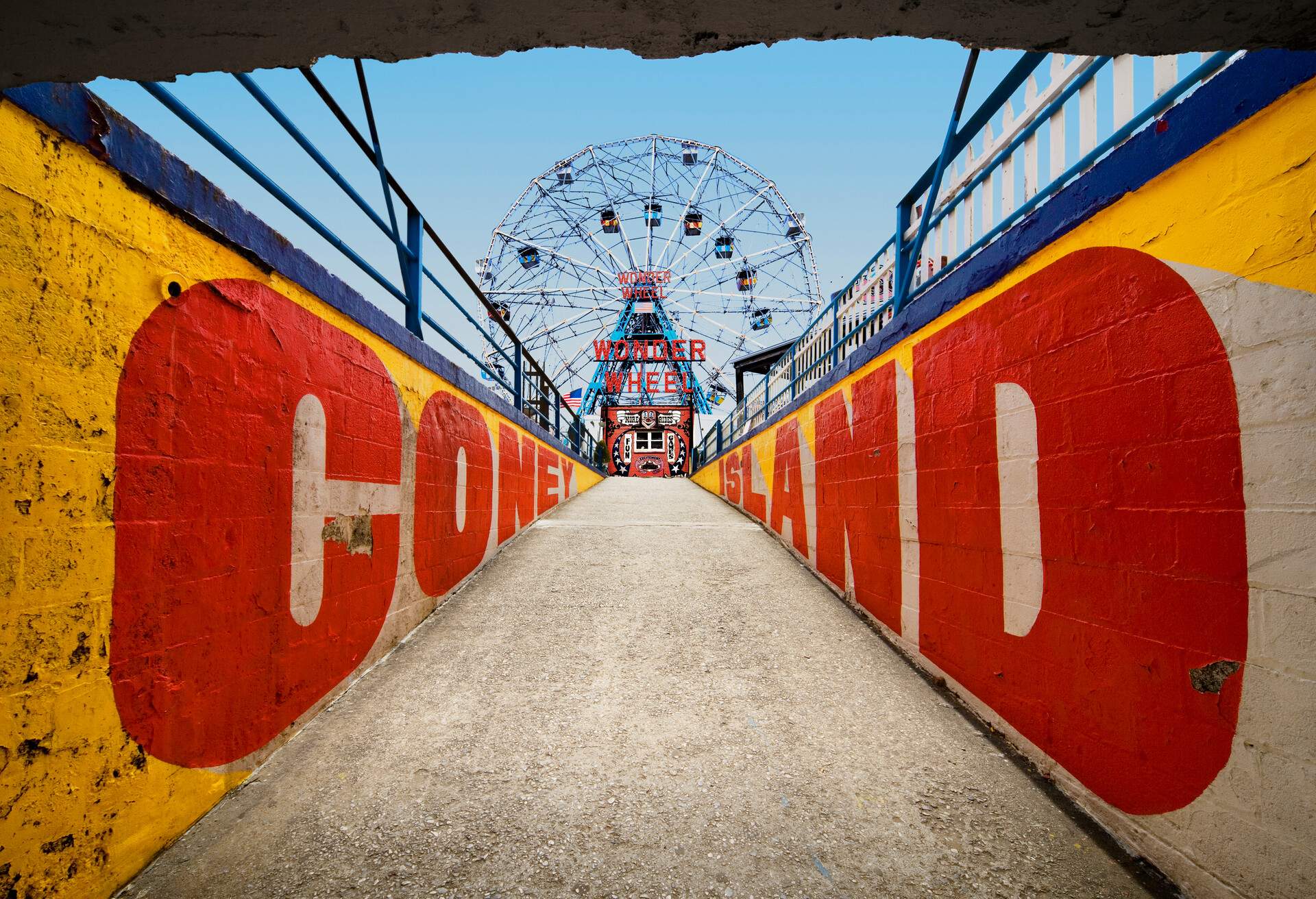A concrete walkway with the words CONEY ISLAND painted on the inner sides of the brick walls and the Wonder Wheel in the distance.